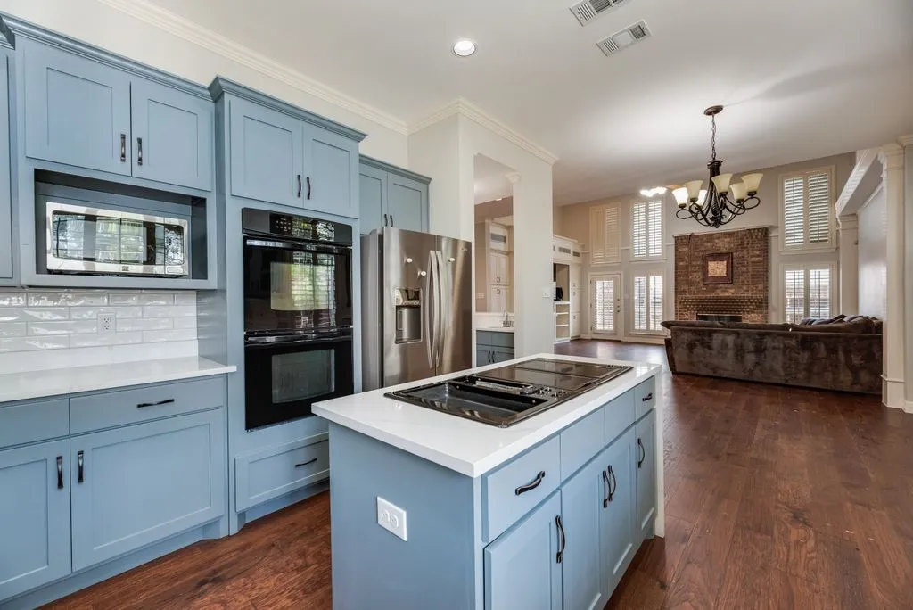 Kitchen showcasing light blue cabinetry, built-in stainless steel appliances, and an island with an integrated cooktop