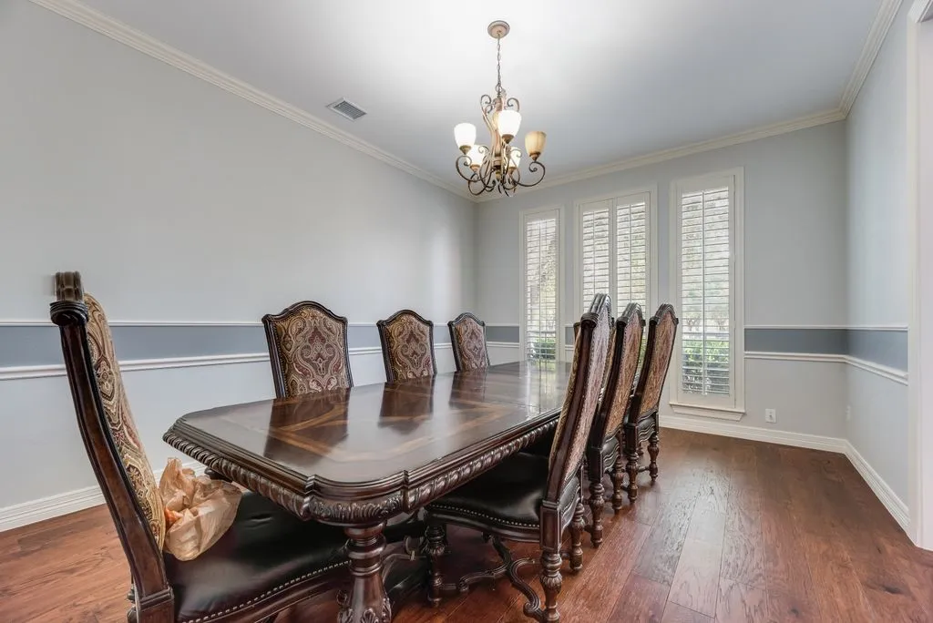 Formal dining space featuring wood-finish flooring, an ornate chandelier, triple windows with plantation shutters, crown molding, and wainscoting