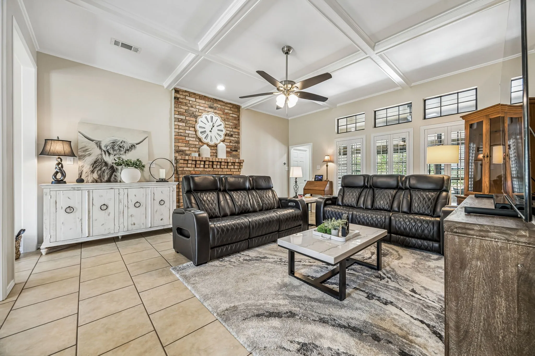 The room boast a striking coffered ceiling, ceiling fan, plantation shutters and stacked windows.
