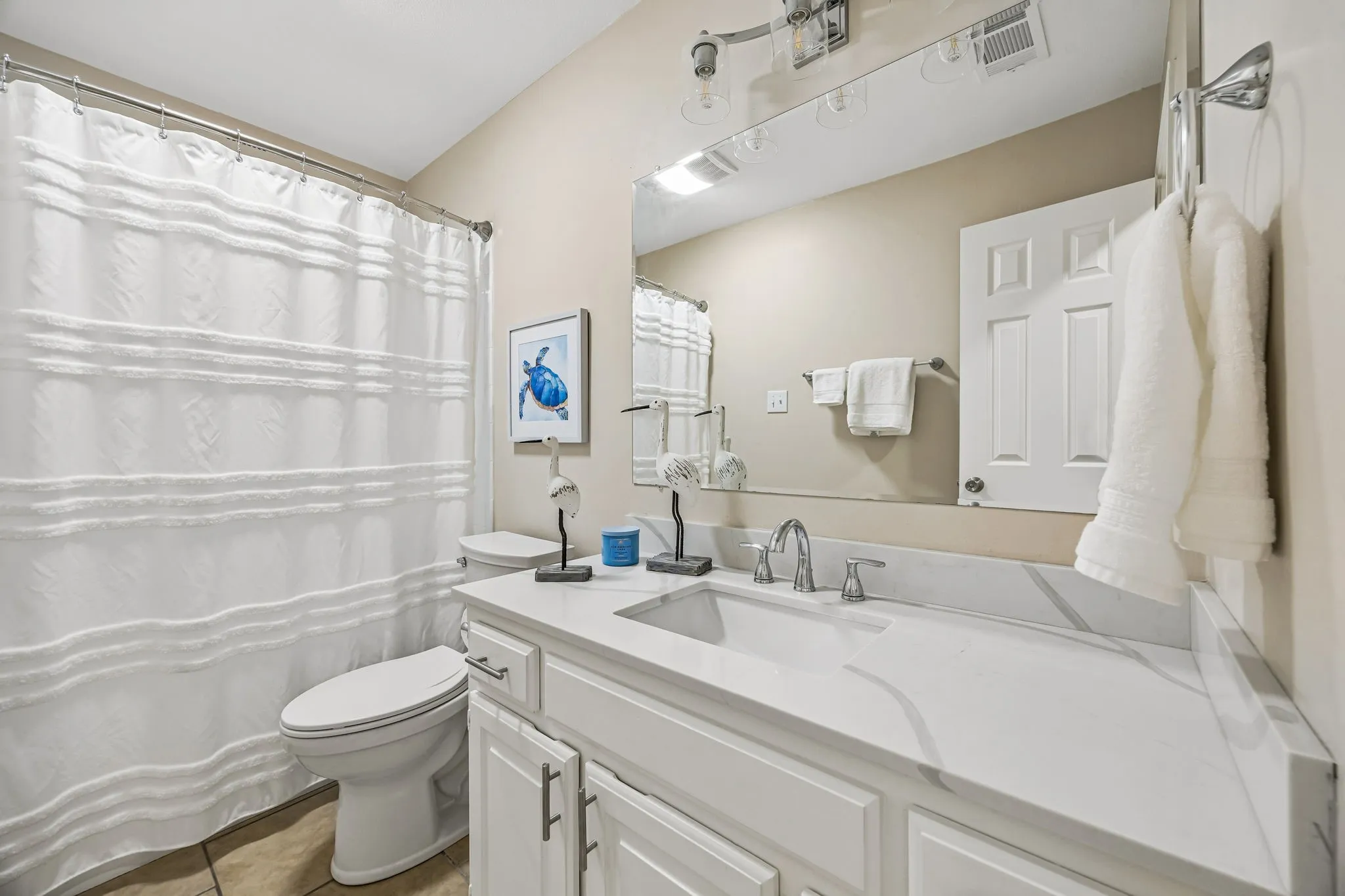 The guest bath has updated vanity with quartz countertop, wave sink and brushed nickel fixtures. Update mirror and light fixture complete the space. The room also boasts tub with shower.