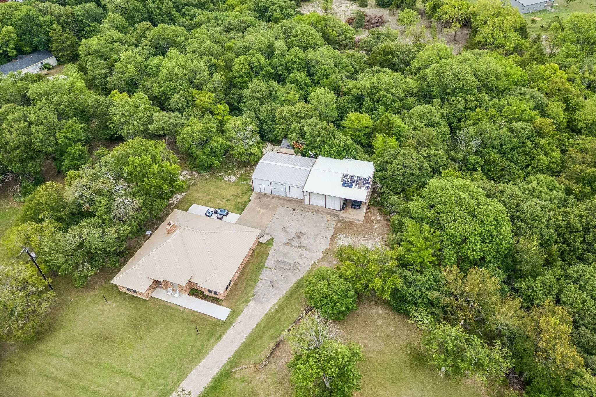 Aerial view looking down on the property shows the metal room on the home, the layout of the driveway and parking areas leading to the workshop and the gorgeous trees that surround the main part of the homestead.