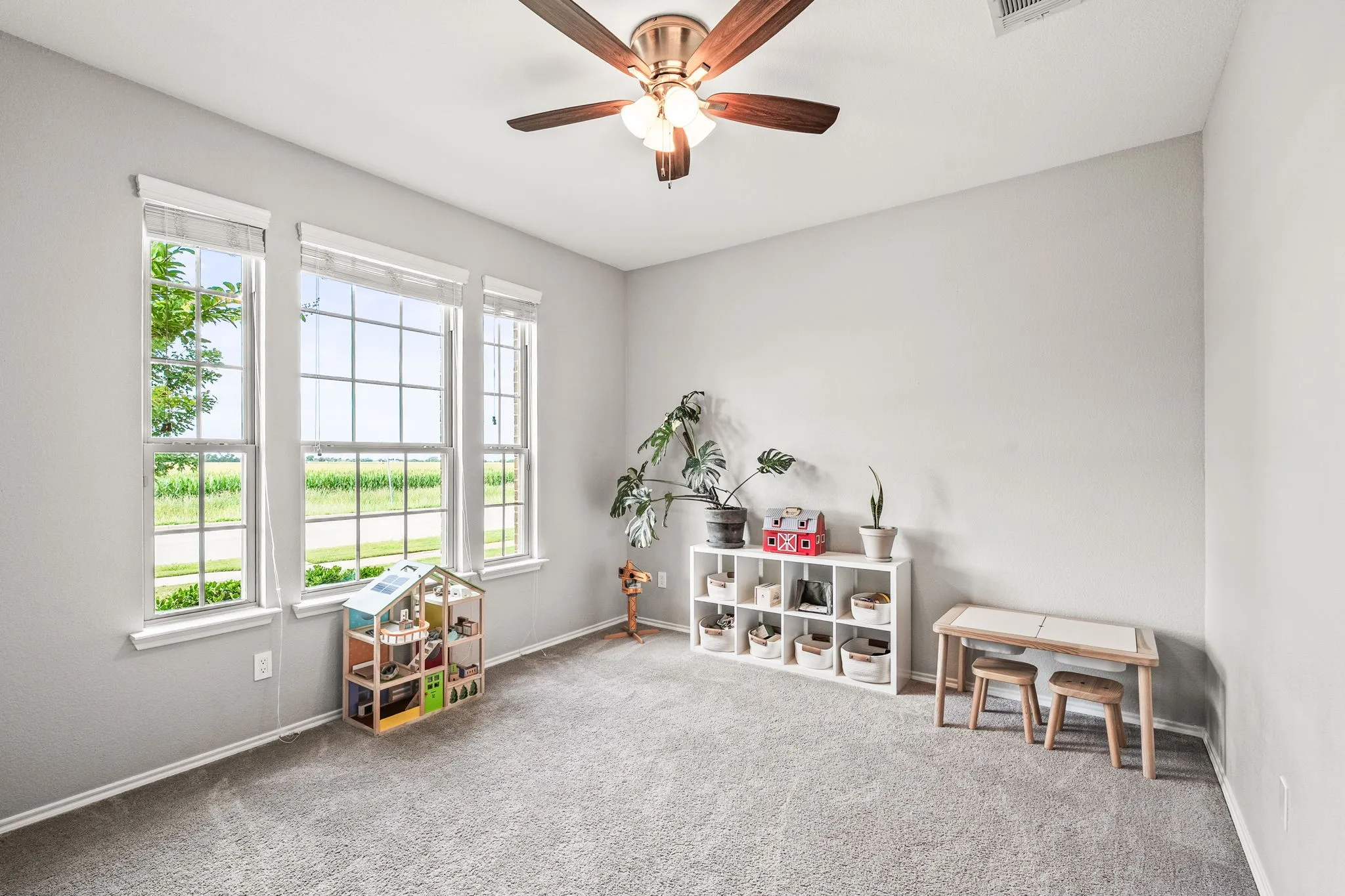 Bright room featuring three double-hung windows with grid patterns, light gray wall paint, gray carpet flooring, and a ceiling fan with light fixture