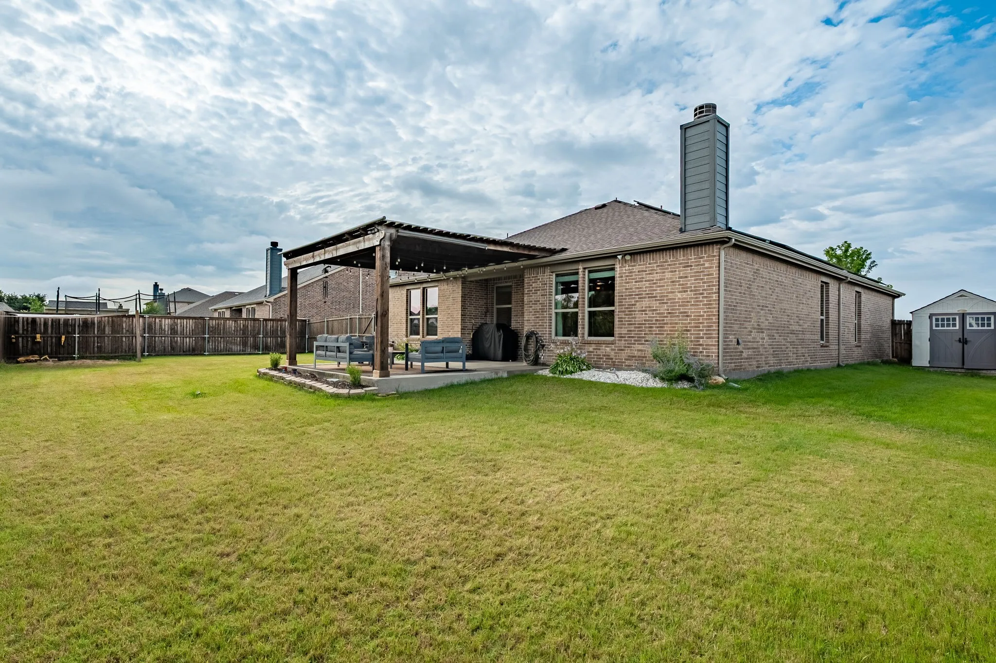 Spacious backyard featuring a covered patio, a full privacy fence, and a utility shed