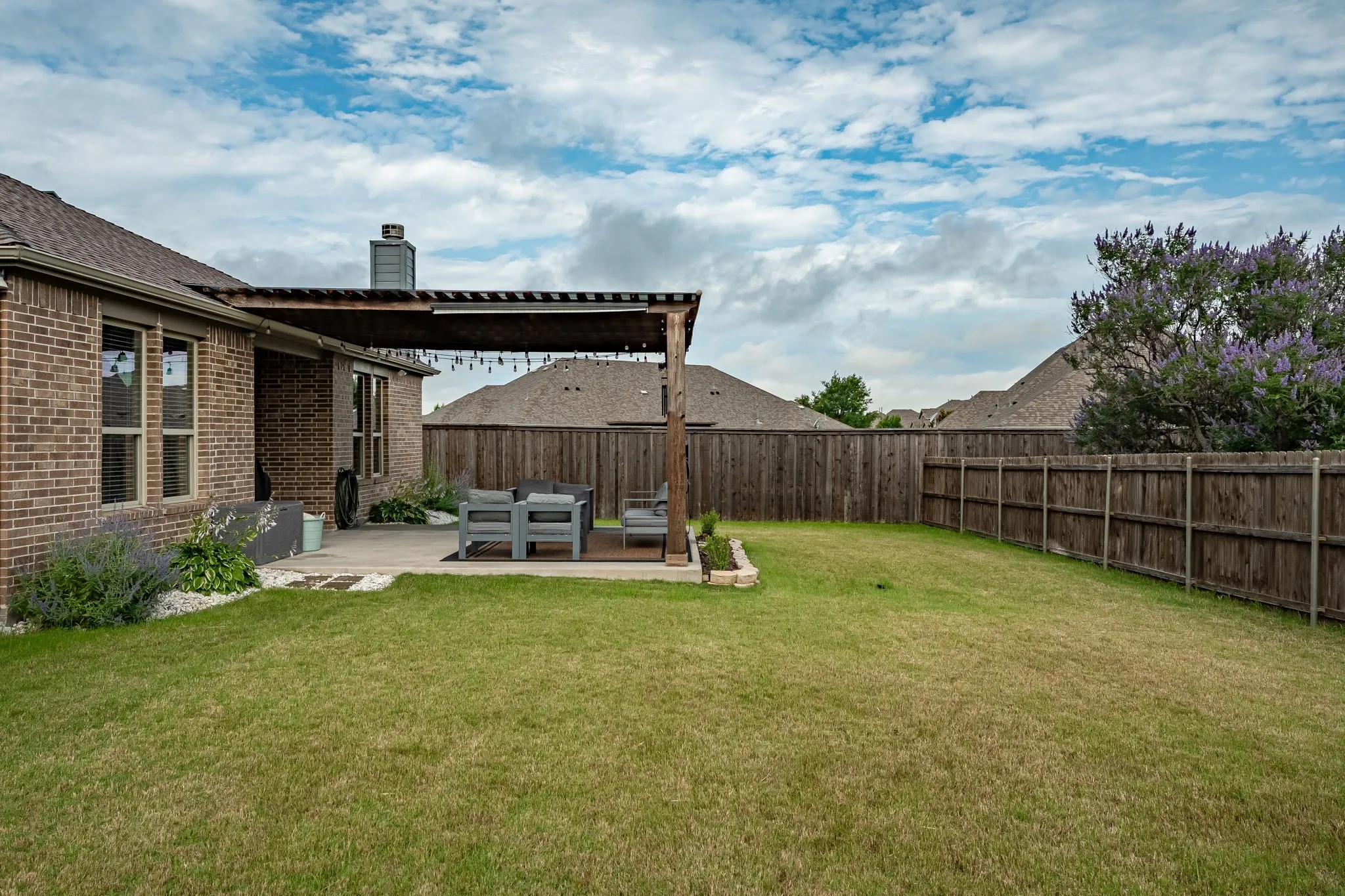 Expansive backyard featuring a wood privacy fence, a mature tree with purple foliage, and a rectangular patio area