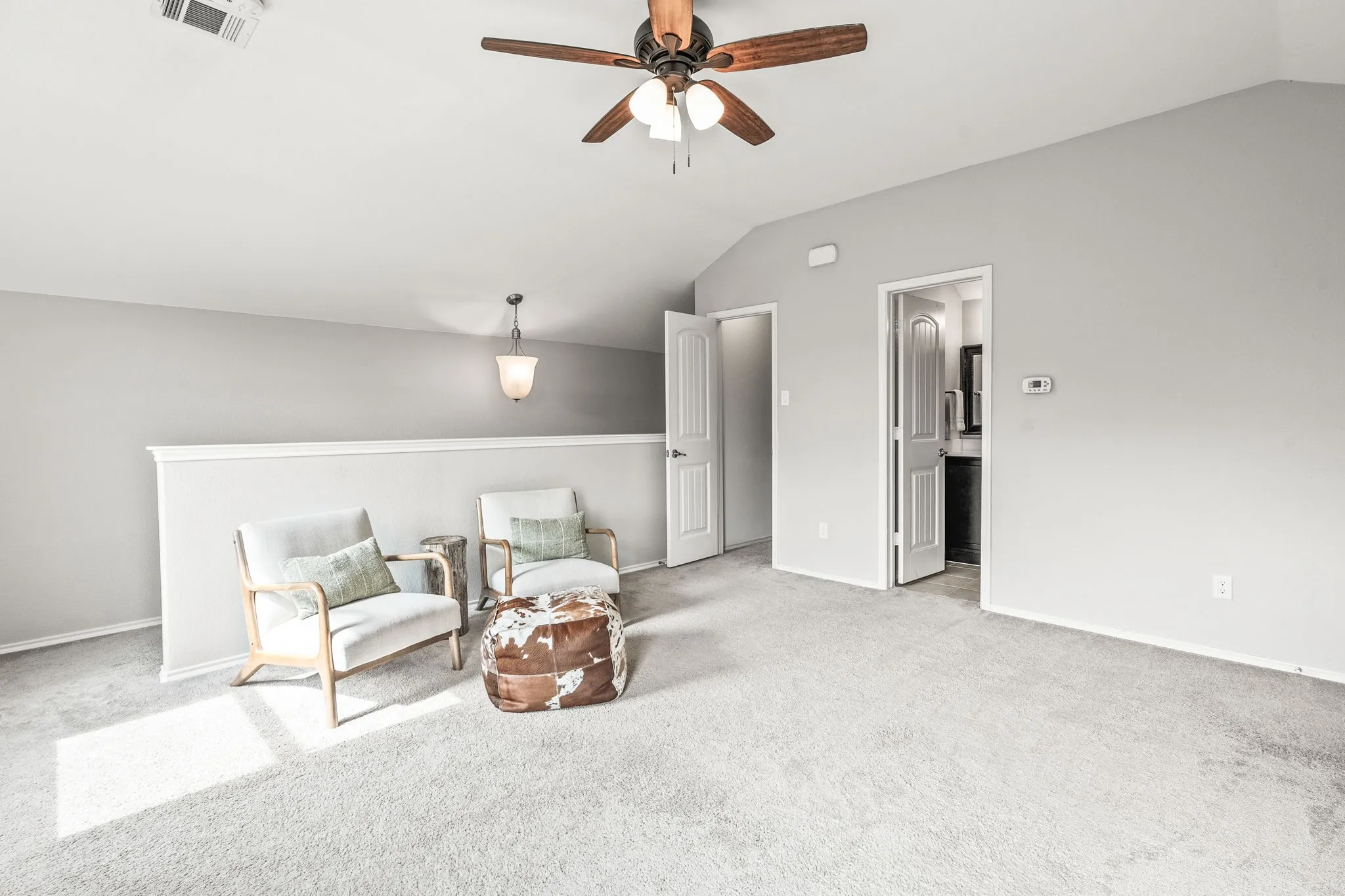 Carpeted loft area featuring a vaulted ceiling with a ceiling fan, a pendant light fixture, and a partial wall railing