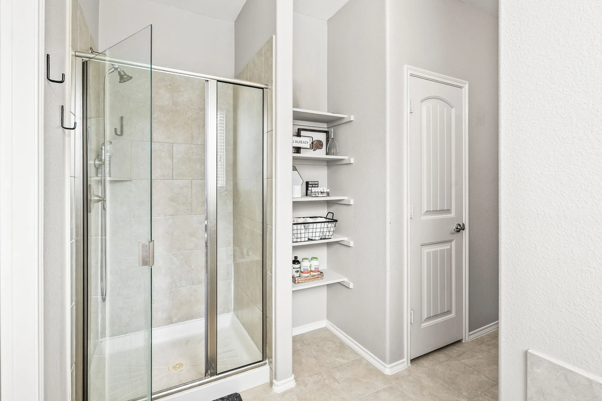 Glass-enclosed shower with tile surround and integrated shelving, featuring brushed nickel hardware