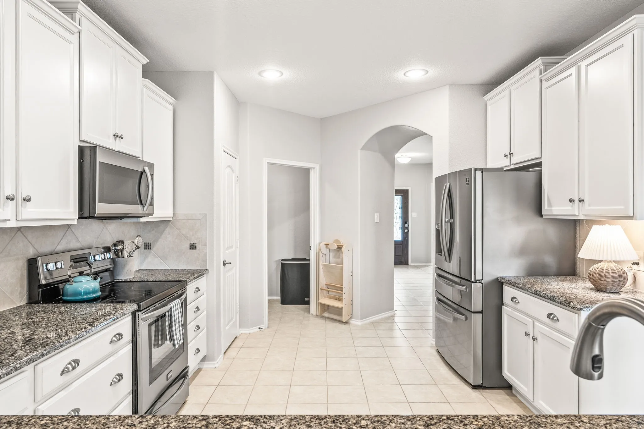Kitchen featuring white cabinetry, granite countertops, tile flooring, stainless steel appliances, and an arched doorway
