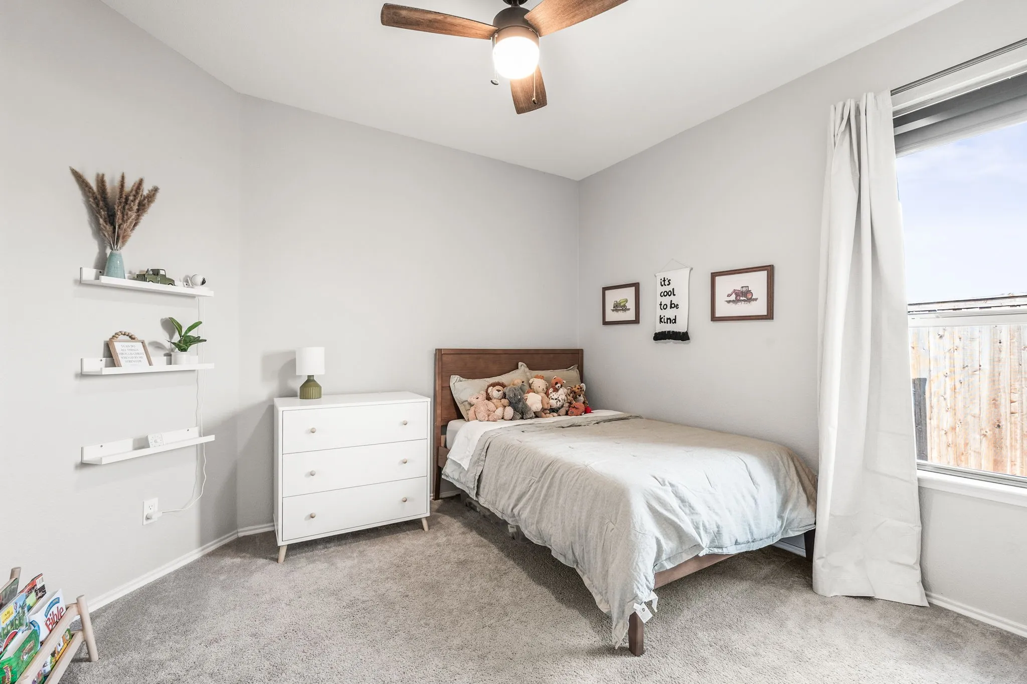 Room featuring light gray wall paint, gray carpeting, a ceiling fan with light fixture, and a window with white curtains