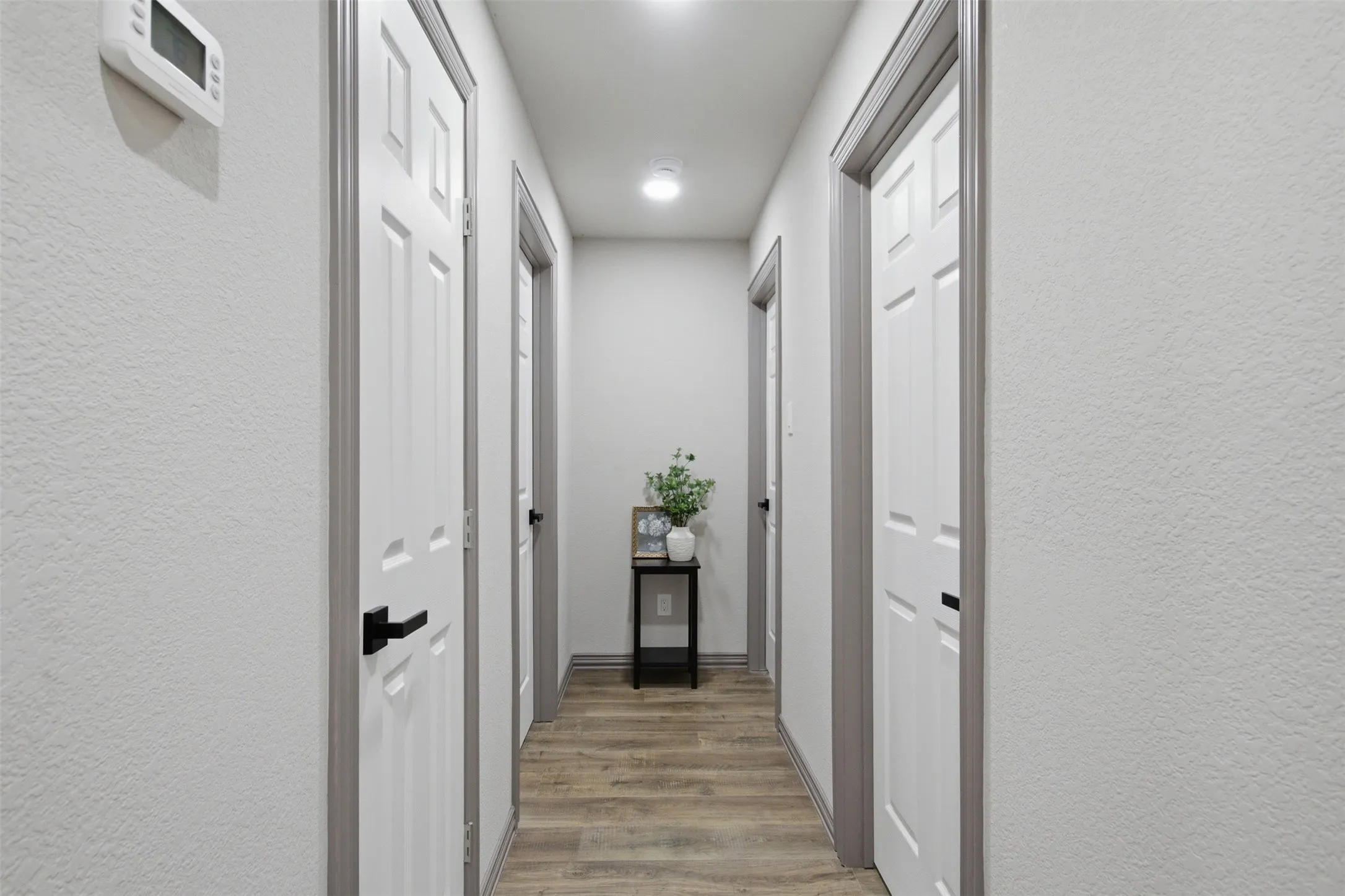 Hallway featuring wood-finish flooring, recessed lighting, and white paneled doors with matte black hardware