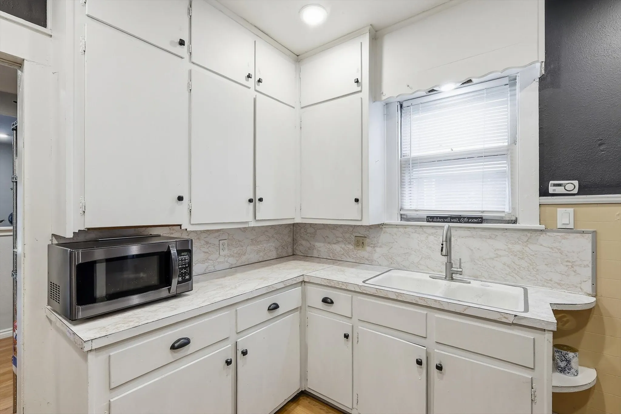 Corner kitchen featuring white cabinetry, light-toned countertops, and a single-basin sink with a gooseneck faucet