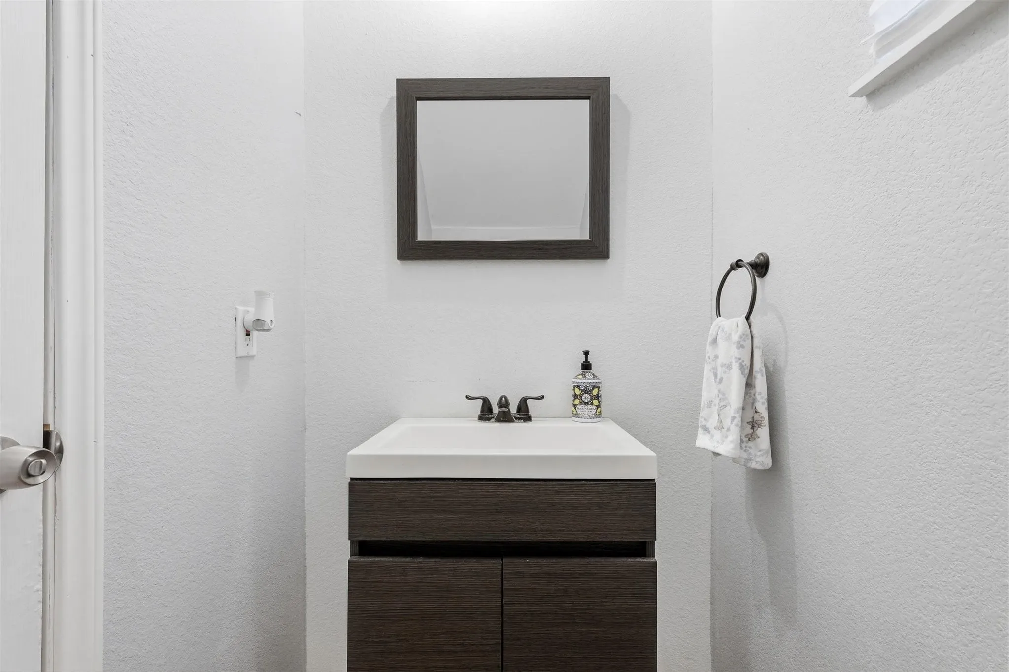 Compact vanity featuring a white integrated sink, dark wood-finish cabinetry, and a framed mirror