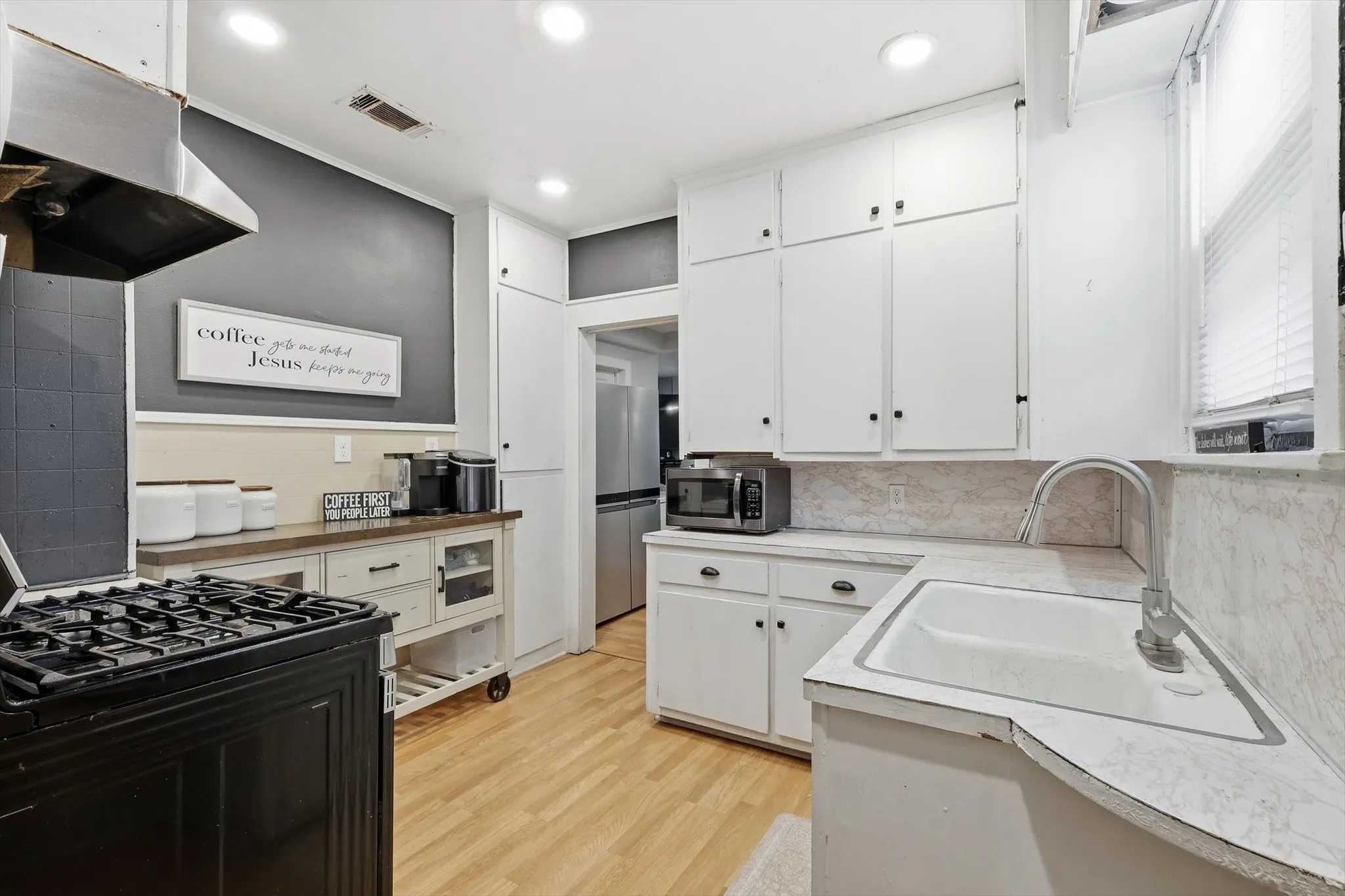 Kitchen featuring light wood-finish flooring, white upper and lower cabinetry, a built-in white sink with a gooseneck faucet, and recessed lighting
