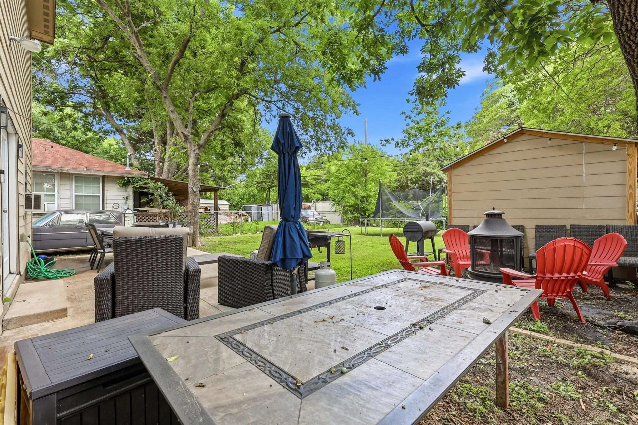 Spacious backyard featuring a concrete patio, mature trees, a storage shed, and a grassy area