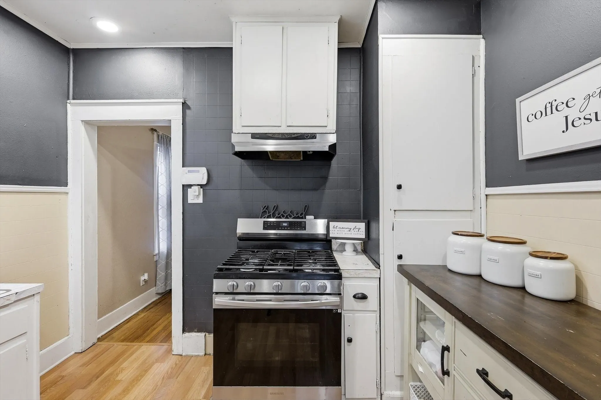 Kitchen featuring a stainless steel gas range, coordinating range hood, white cabinetry, dark wood-finish countertops, and wood-finish flooring