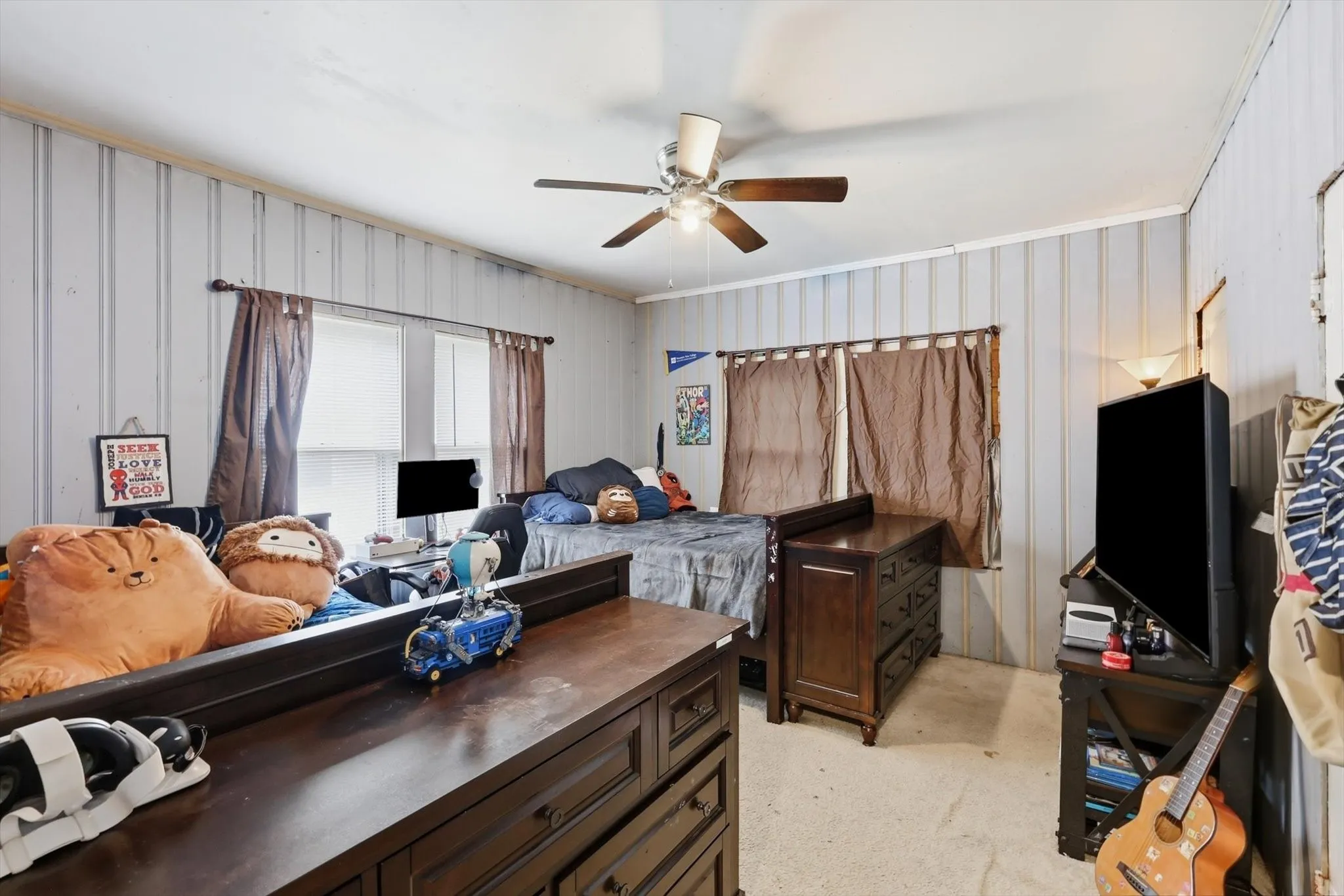 Room featuring light-colored vertical paneling, two windows with curtain rods, and a ceiling fan with light fixture