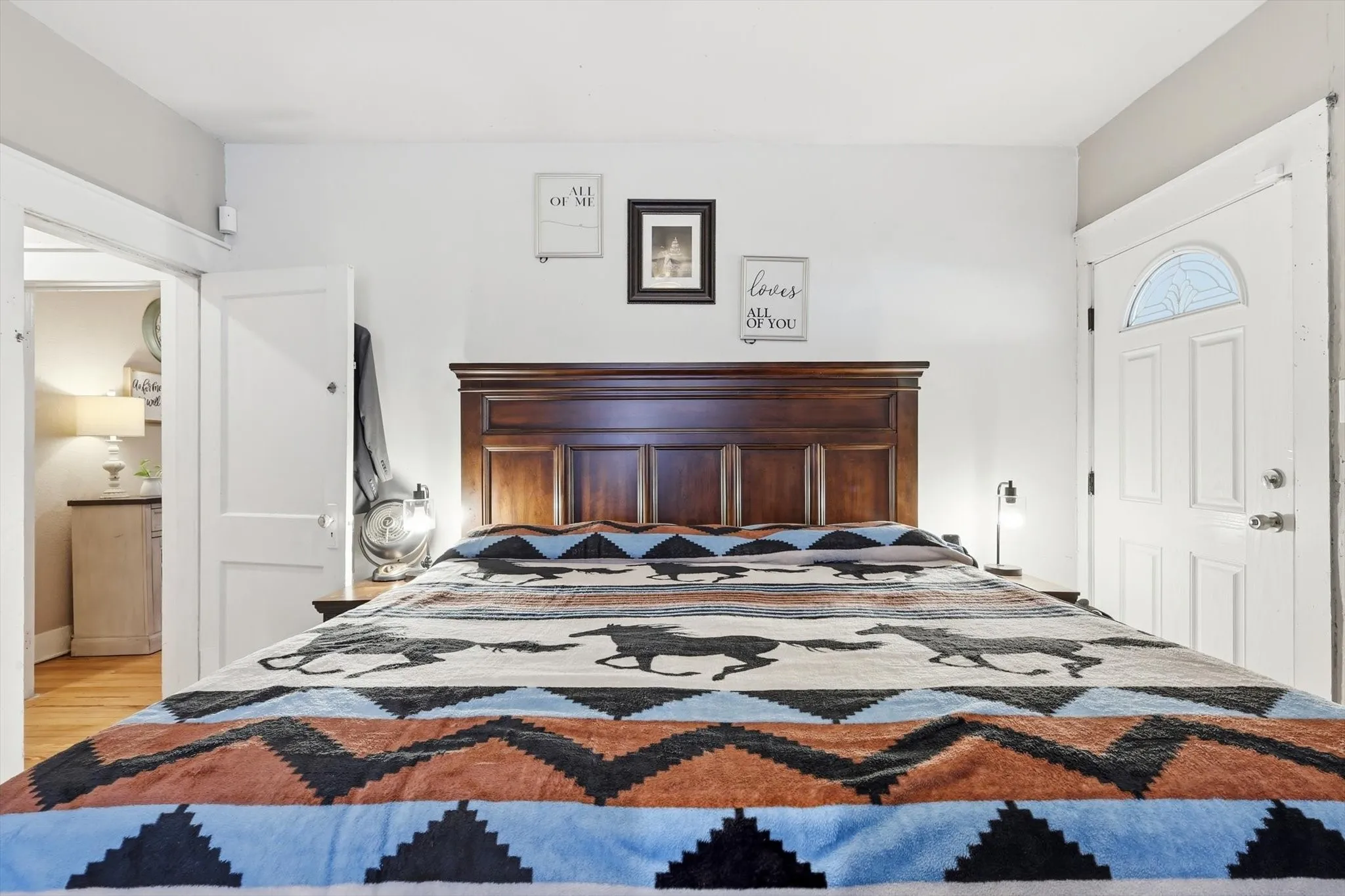 Bedroom with wood-finish flooring, a solid wood headboard, a white interior door, and a white exterior-style door with an arched decorative glass insert
