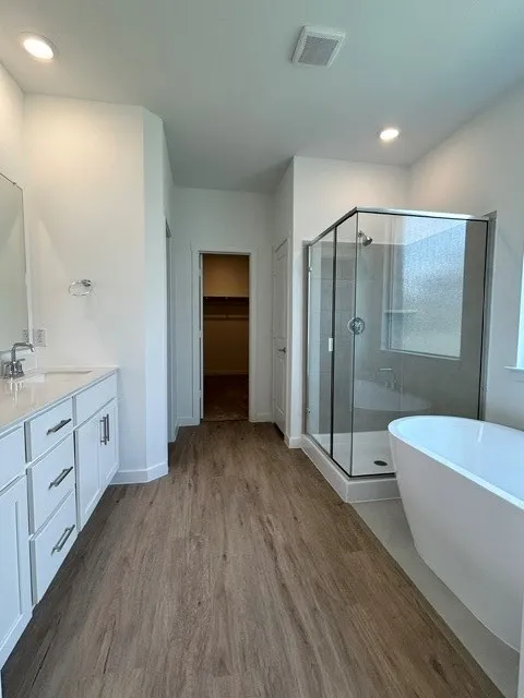 Spacious bathroom featuring a freestanding tub, glass-enclosed shower, dual vanity with white cabinetry, and wood-finish flooring