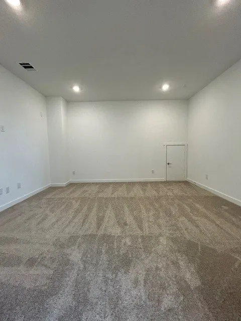 Spacious room featuring new carpeting, recessed lighting, white walls, white baseboards, and a white interior door