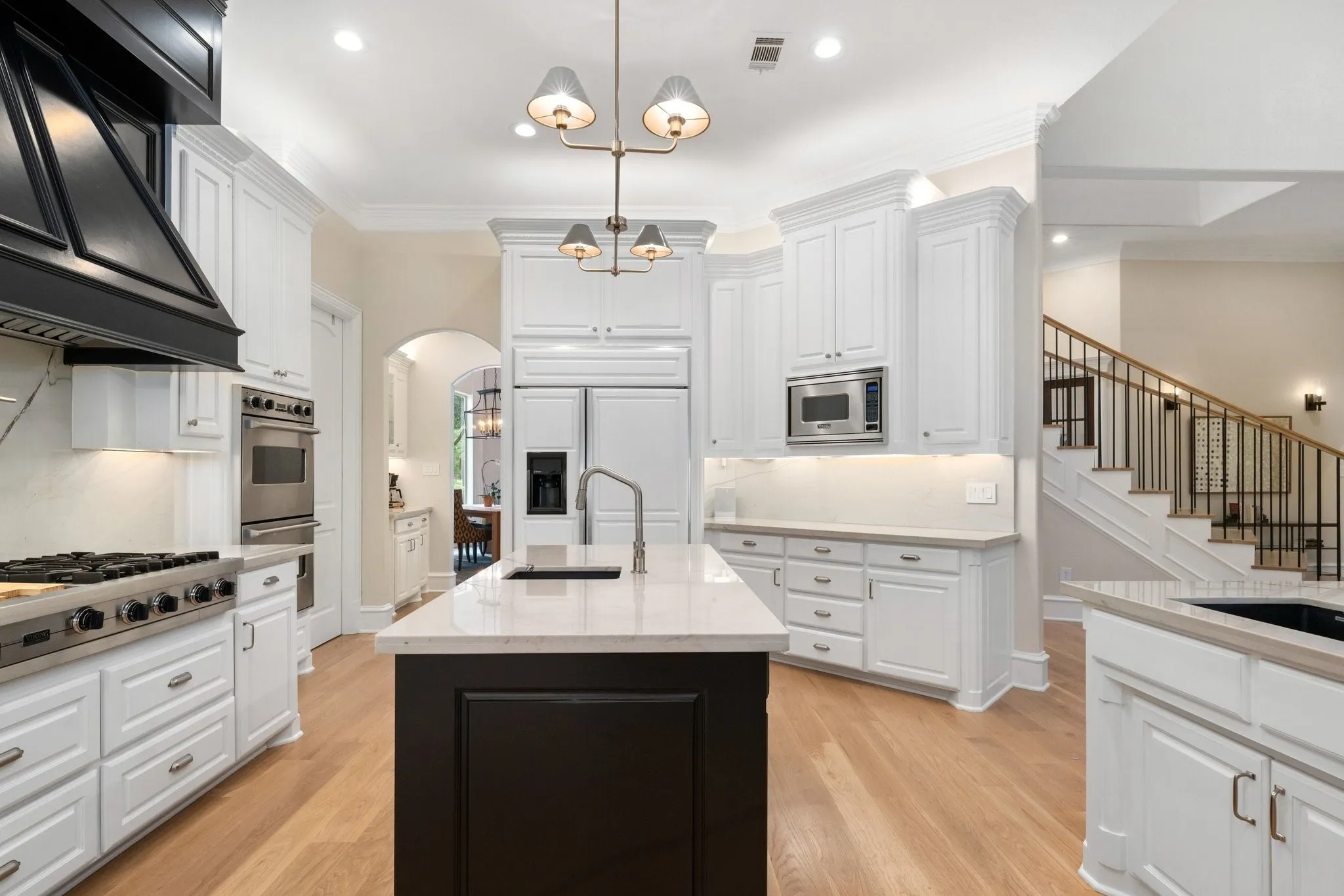 Kitchen featuring a central island with a sink, white cabinetry, stainless steel appliances, a black range hood, and light wood-finish flooring