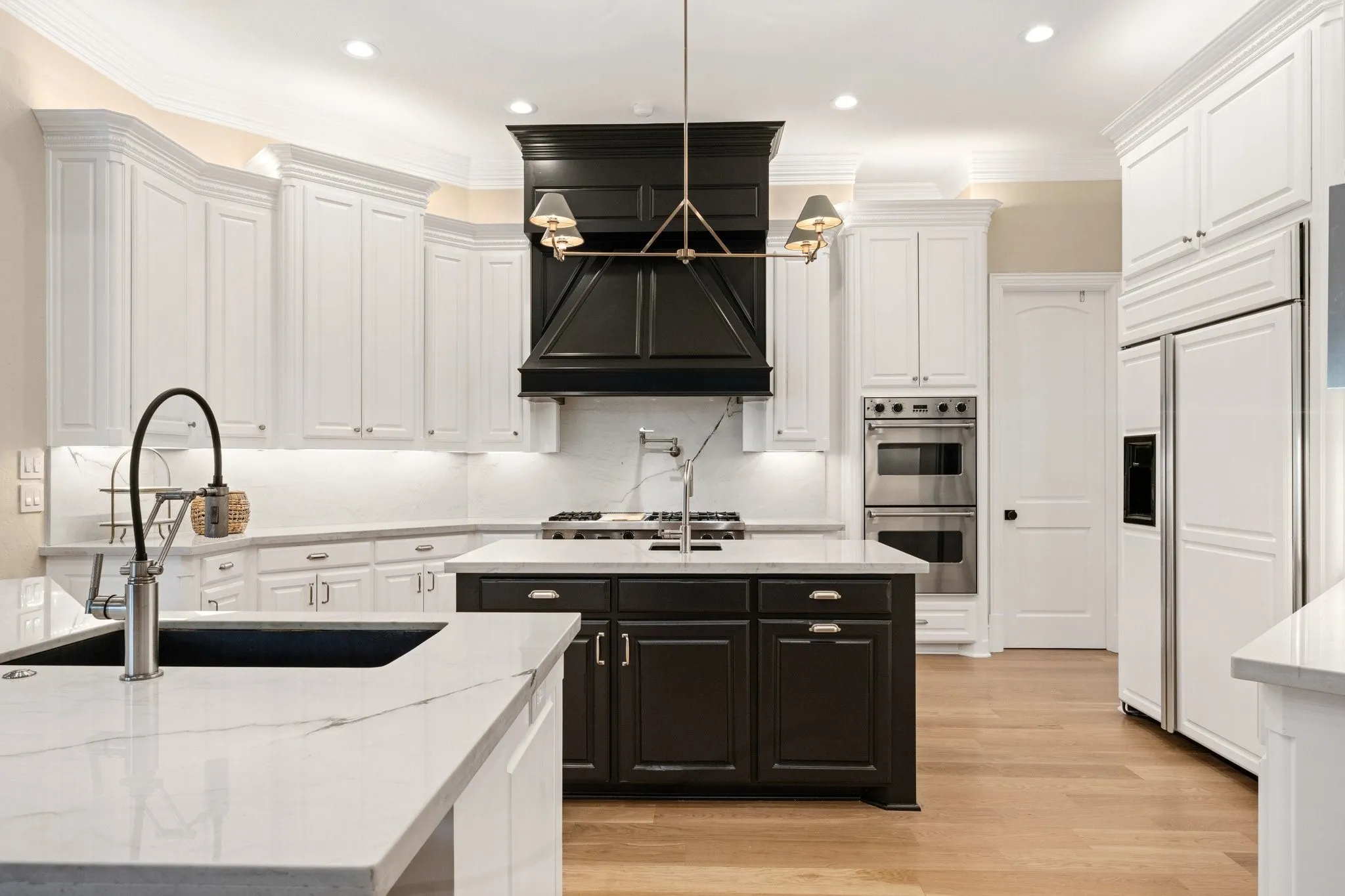 Bright kitchen featuring white perimeter cabinetry, a contrasting dark island with an integrated sink, polished chrome fixtures, and light-toned wood-finish flooring