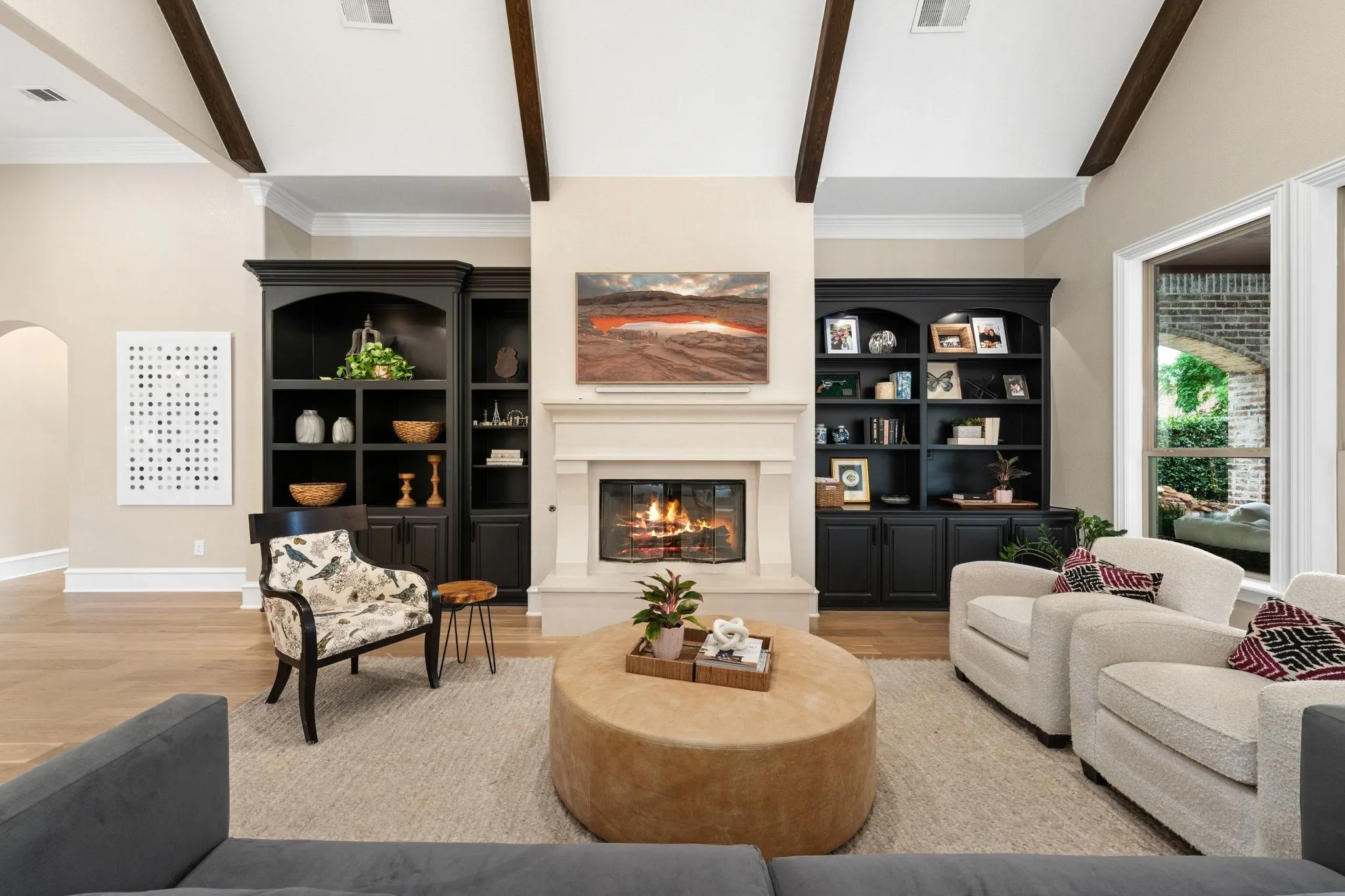 Living space featuring a prominent fireplace with a substantial mantel, dark built-in cabinetry flanking the fireplace, exposed ceiling beams, light wood-finish flooring, and crown molding