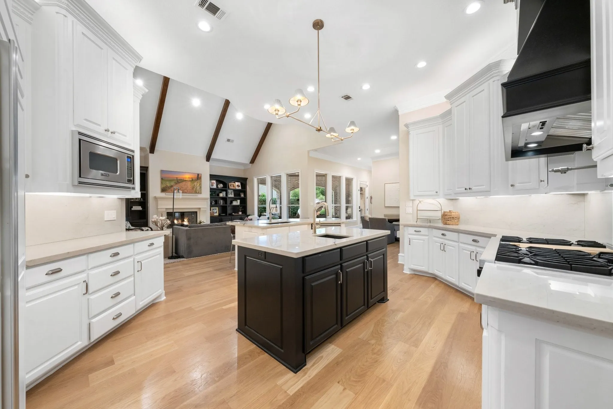Bright kitchen featuring white cabinetry, a dark island with a light-toned countertop, and light wood-finish flooring