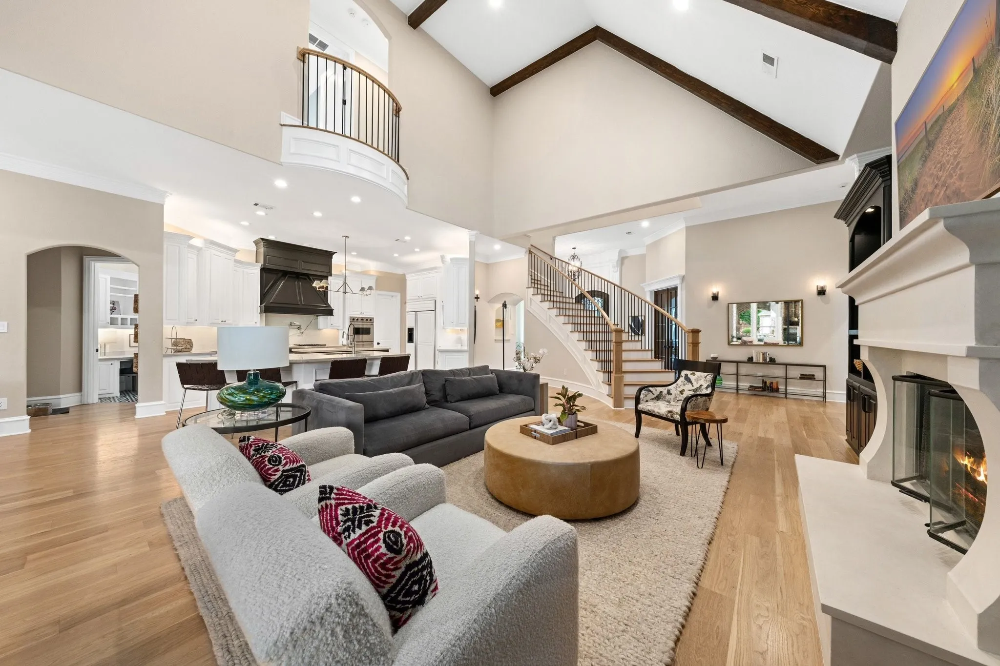 Expansive living area featuring soaring vaulted ceilings with exposed wood beams, a prominent stone fireplace with glass-fronted firebox, and light wood-finish flooring