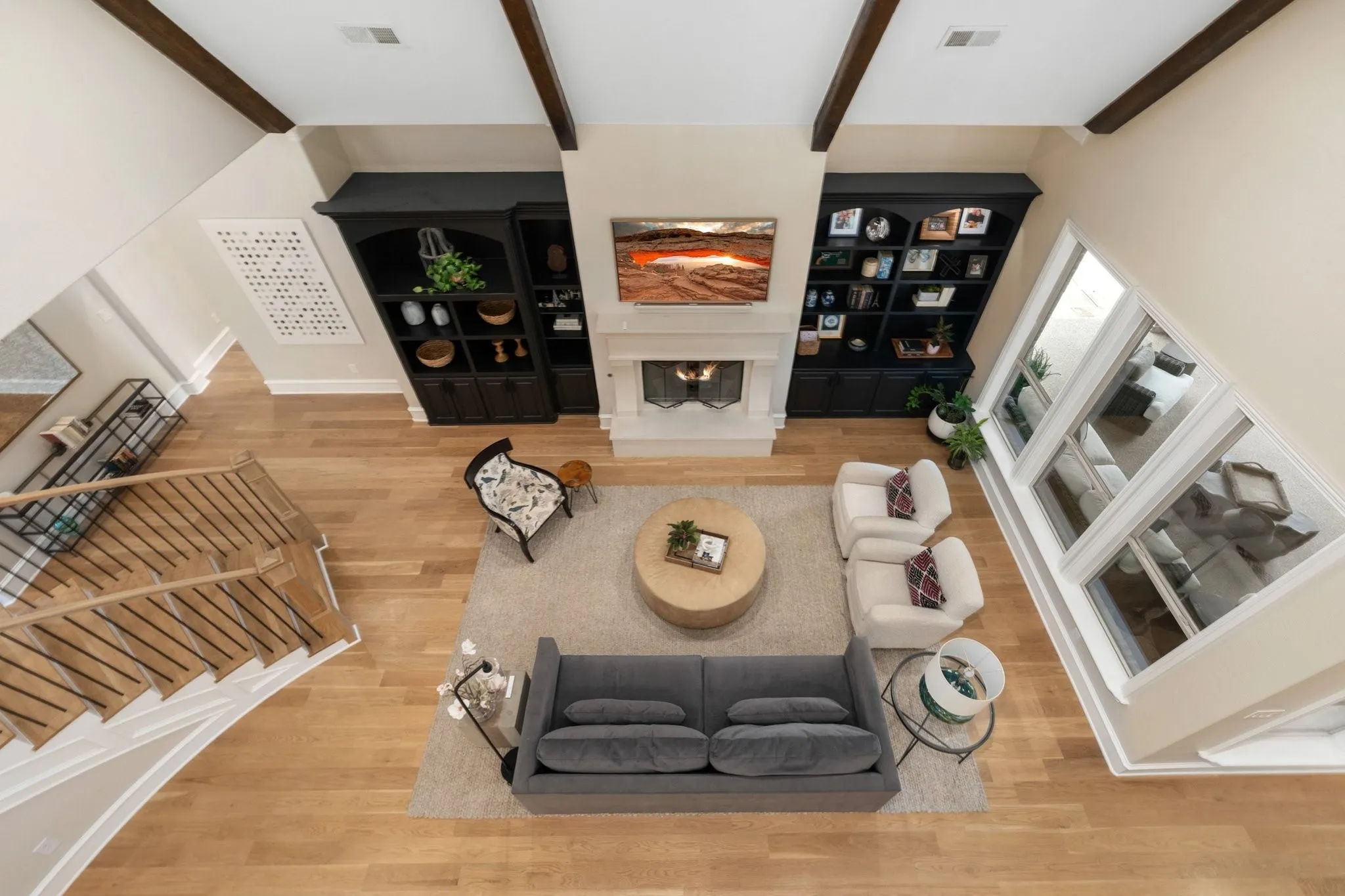 Vaulted living area featuring exposed ceiling beams, a central fireplace with a mantel, built-in cabinetry, expansive windows, and wood-finish flooring