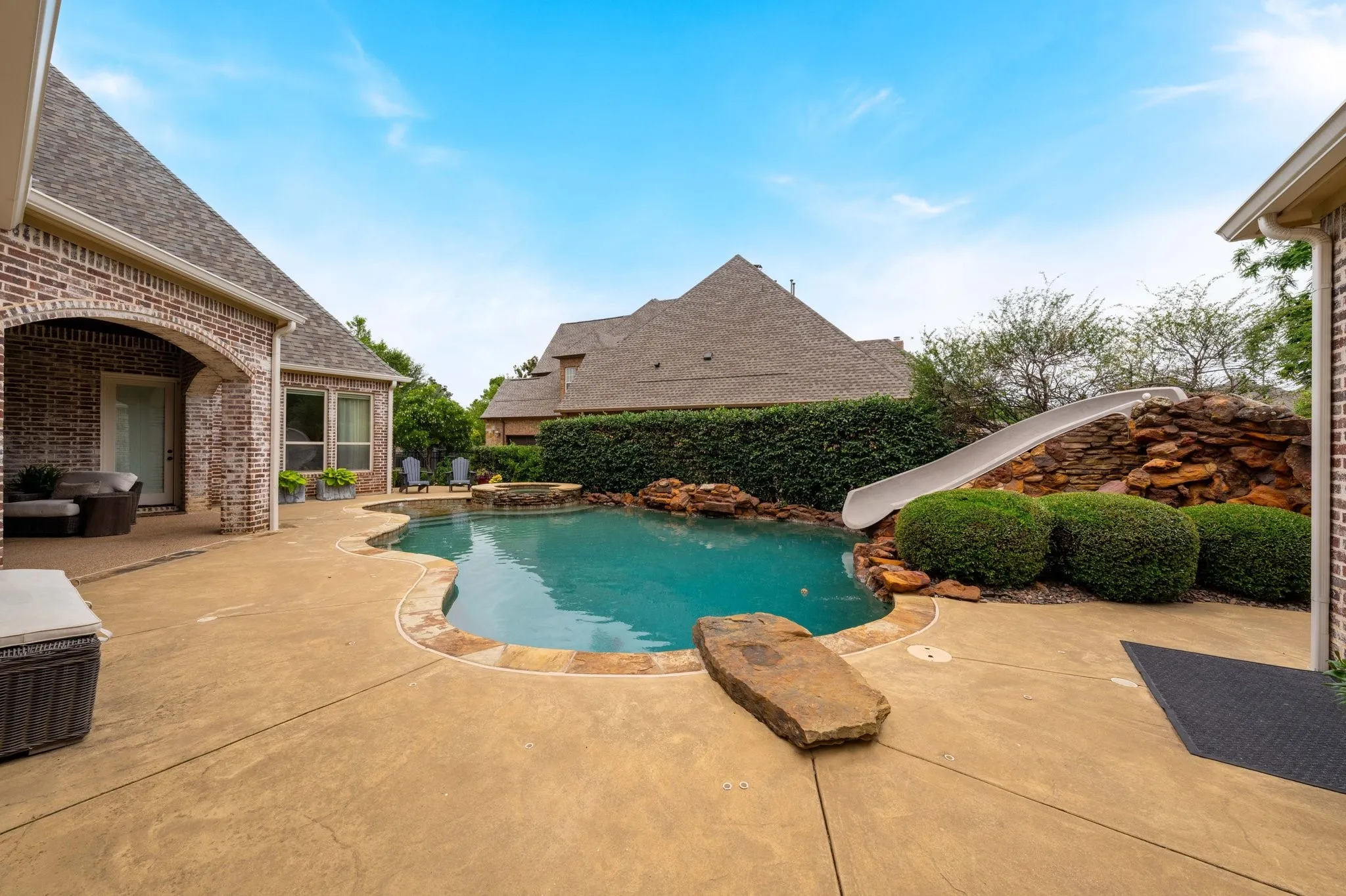 Curved swimming pool with rock waterfall feature and integrated slide