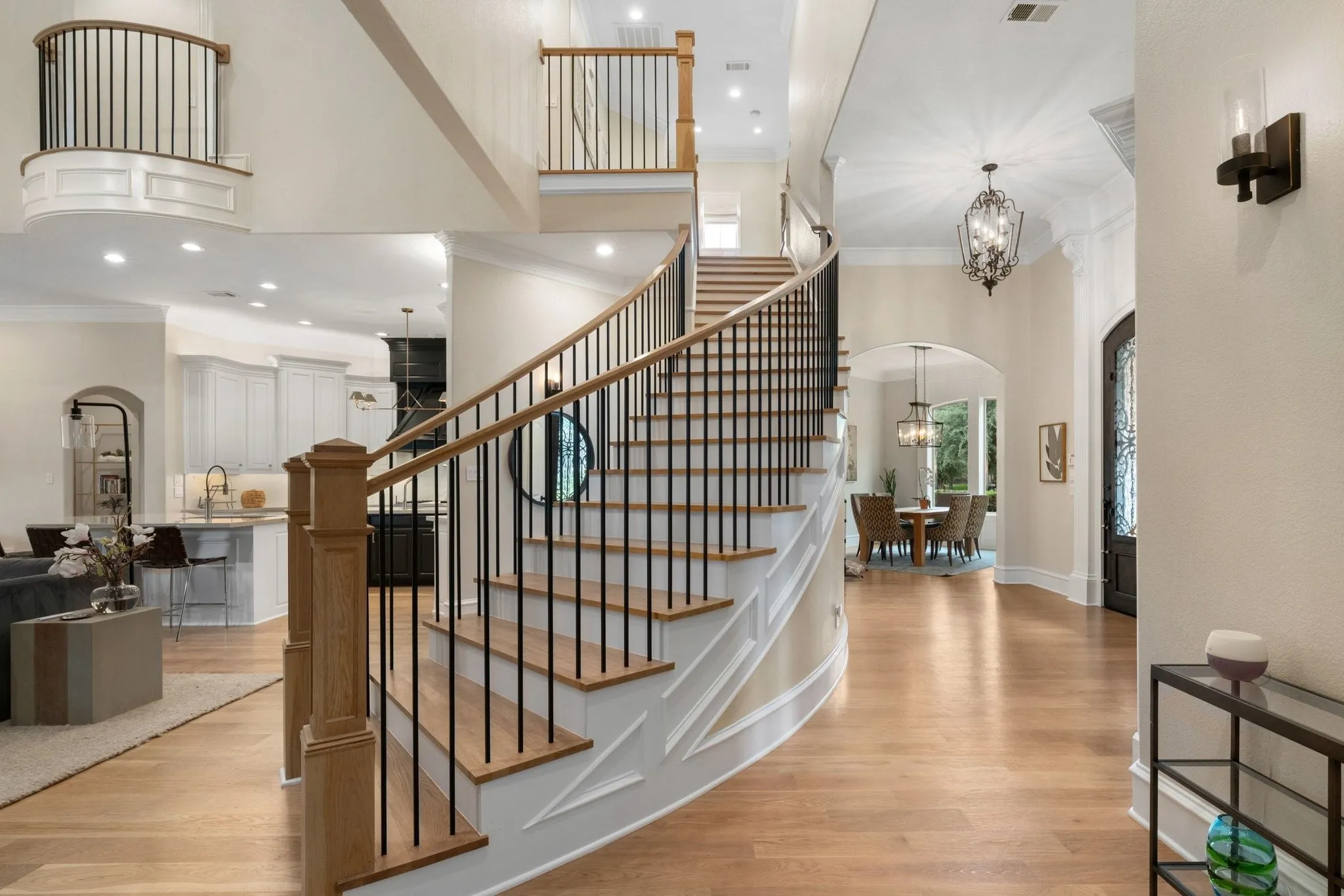 Elegant curved staircase with wood-finish treads and risers, featuring a black wrought iron baluster system and natural wood handrail