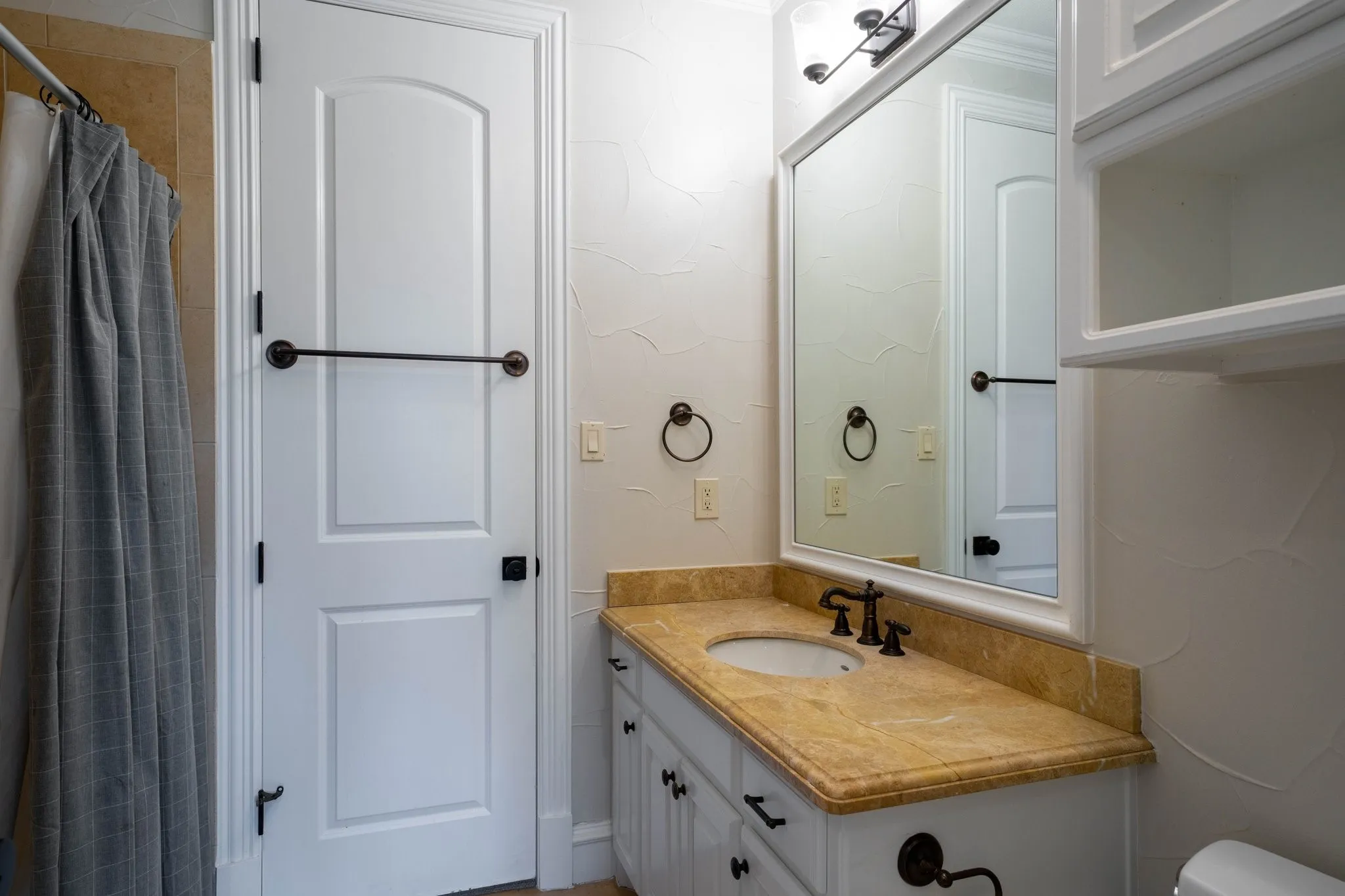 Bathroom featuring a single vanity with a golden-hued countertop and under-mount sink
