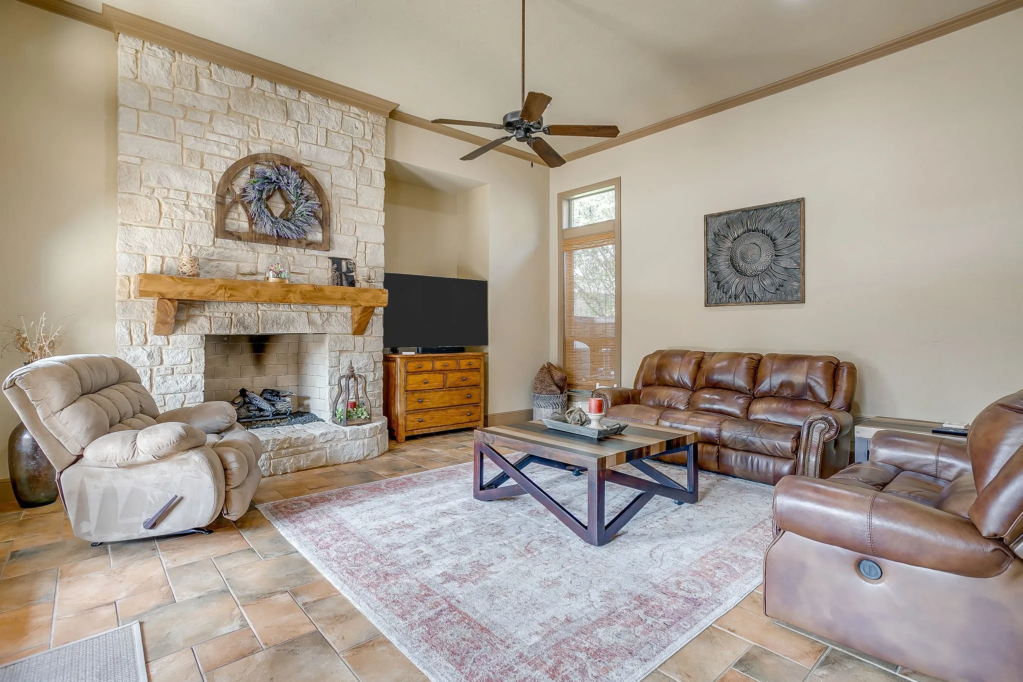 Living area featuring a stone fireplace with a wood mantle, vaulted ceiling, and a ceiling fan