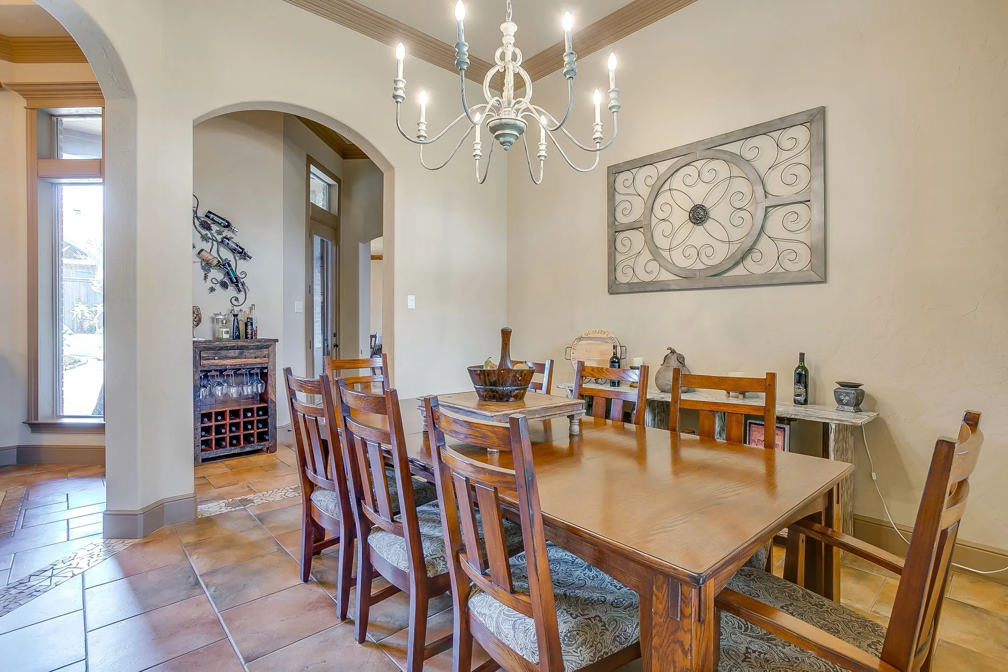 Formal Dining area off entry and kitchen featuring large format tile flooring with decorative inlay, arched passageways, a candelabra-style chandelier, and a decorative tray ceiling