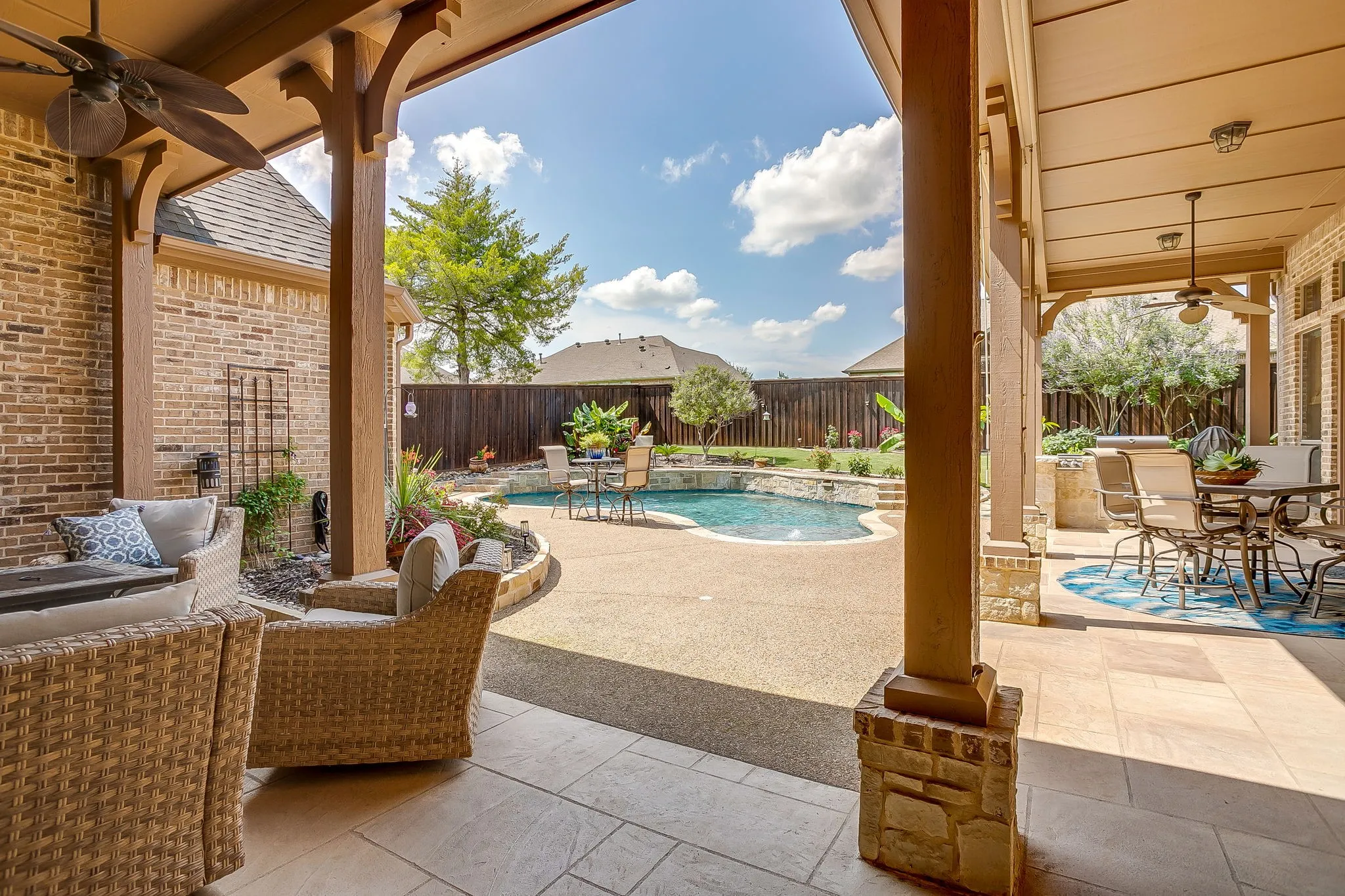 Expansive covered patio featuring a built-in outdoor kitchen, recessed lighting, ceiling fans, and stone-accented columns