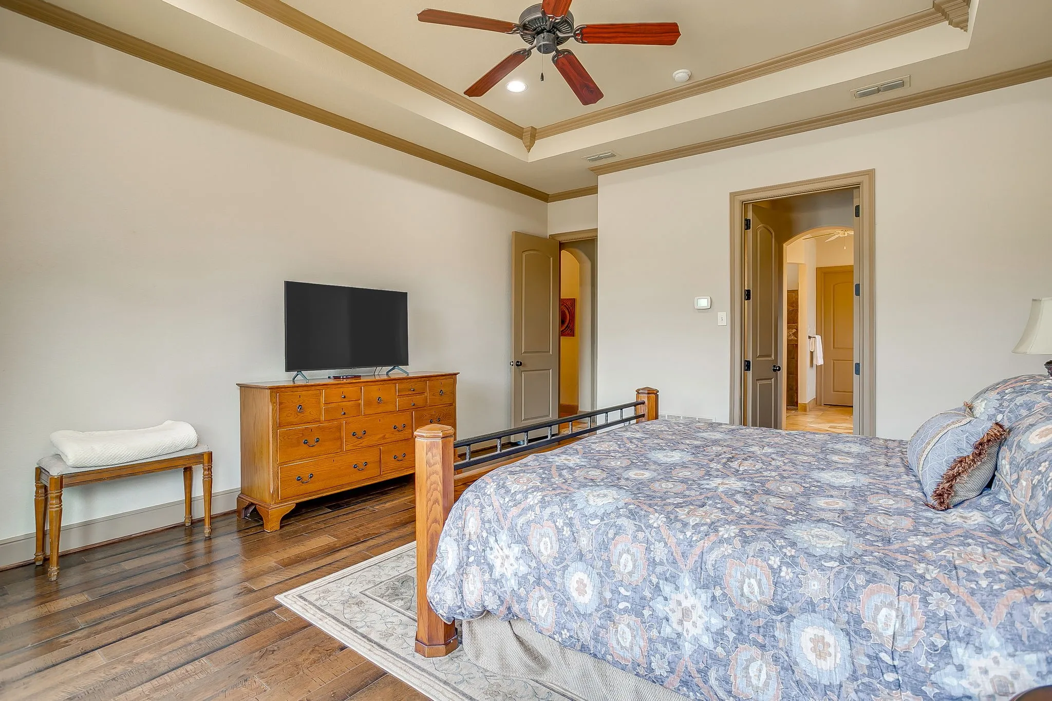 Spacious Primary Bedroom featuring wood-finish flooring and a tray ceiling with crown molding