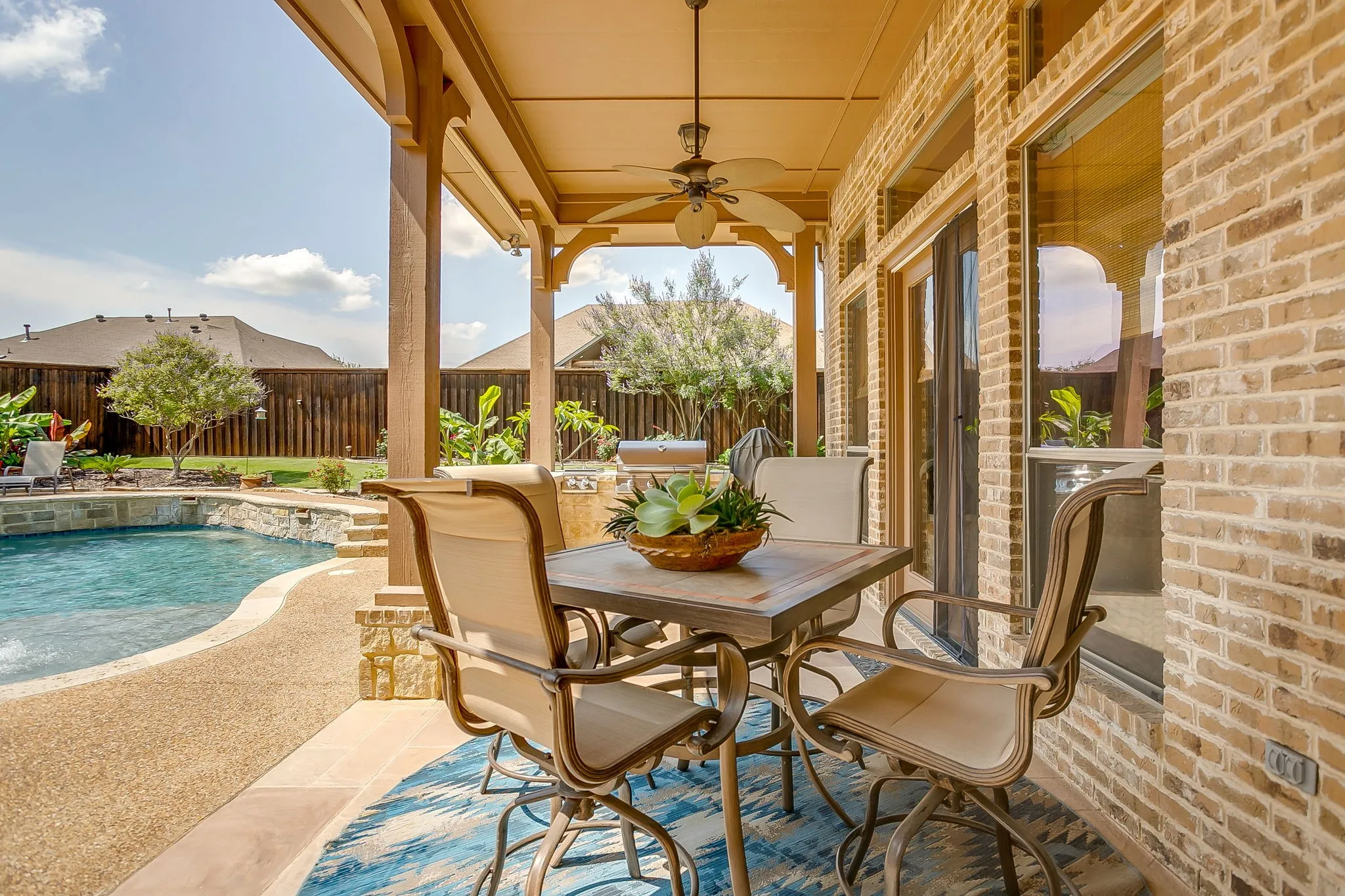 Covered patio featuring a ceiling fan, light-toned brick exterior, large glass doors, and exposed aggregate patio flooring