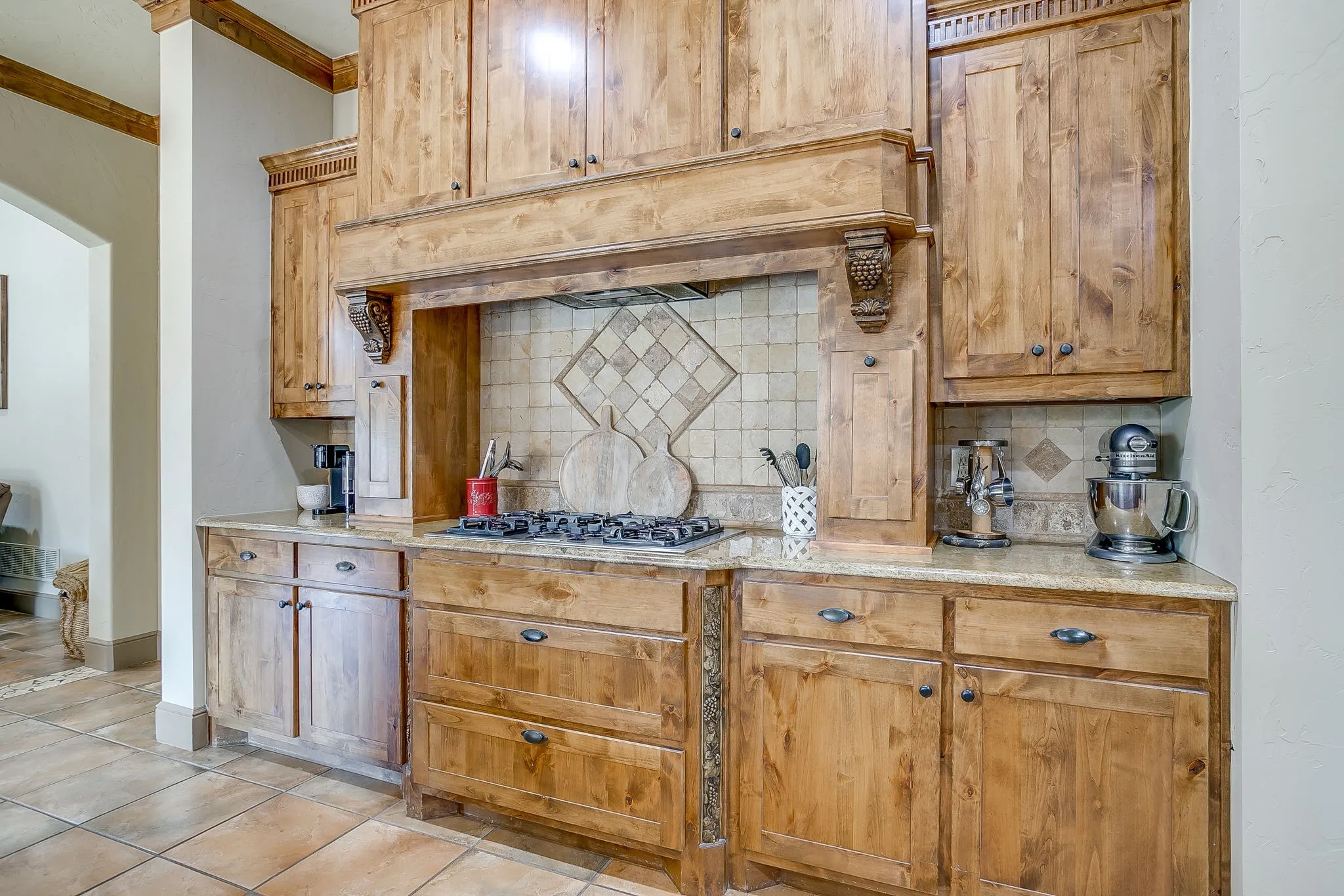 Warm wood cabinetry with dark hardware, a built-in gas cooktop, and a custom range hood
