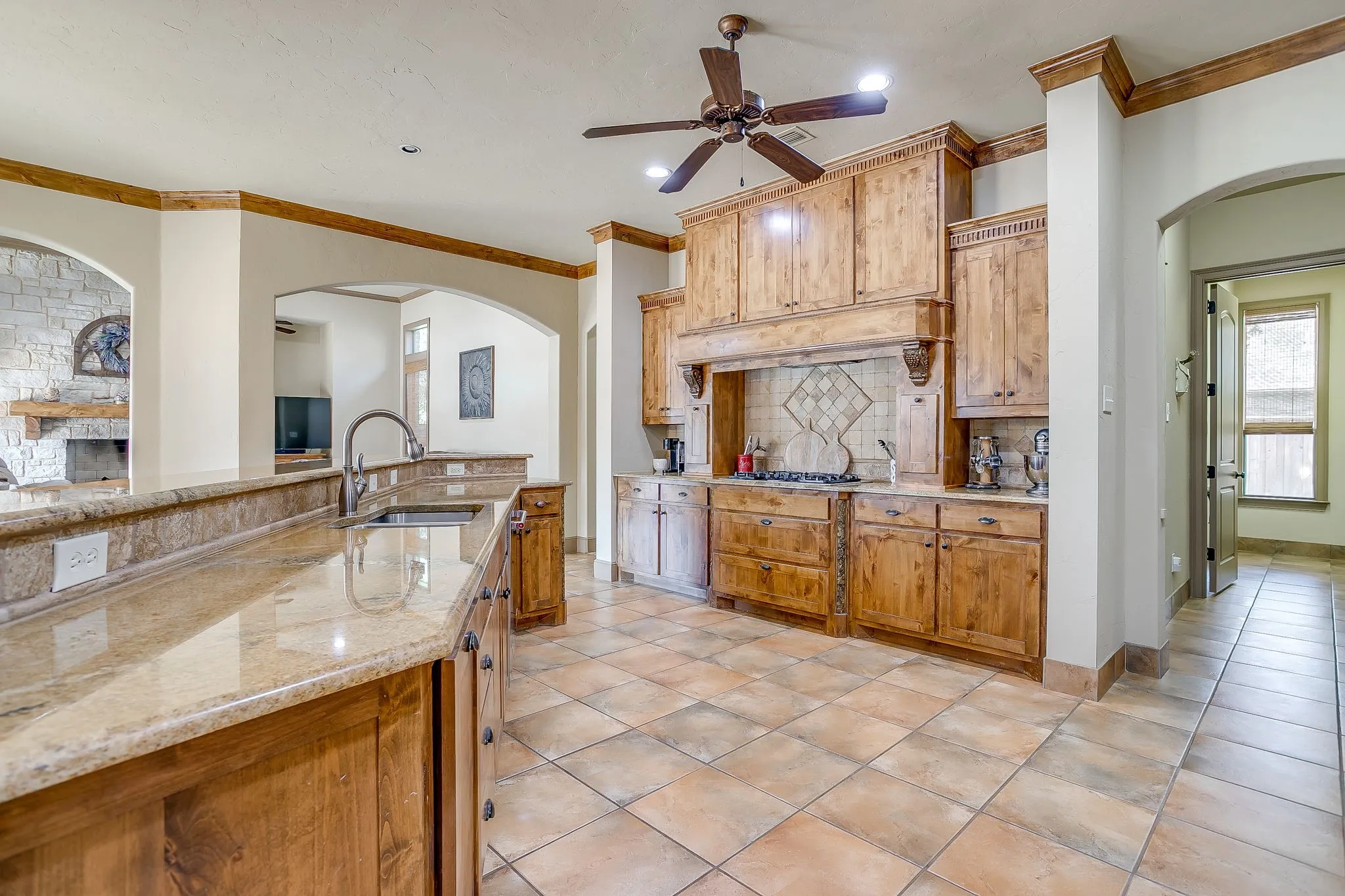 Kitchen featuring custom wood cabinetry, stone countertops, a tile backsplash, and a ceiling fan
