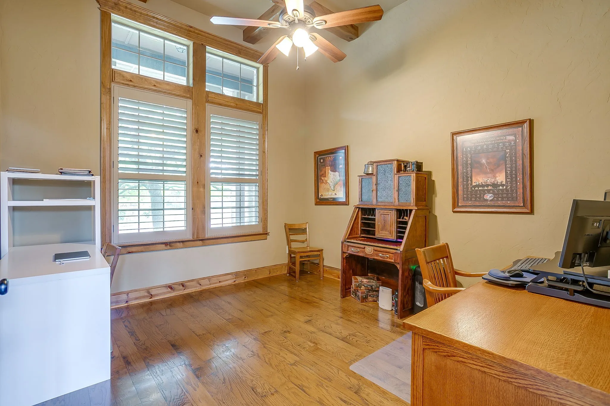 Tall windows with natural wood trim and plantation shutters, wood-finish flooring, vaulted ceiling, and a ceiling fan with light fixture