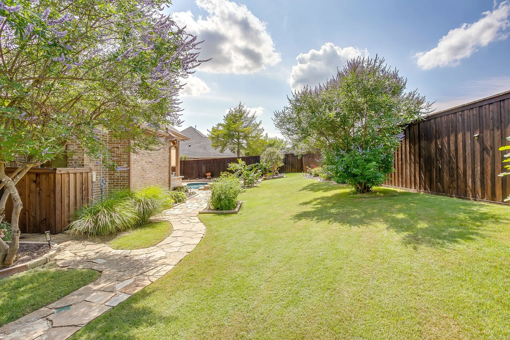 Expansive backyard featuring a lush lawn, mature trees, and a flagstone pathway