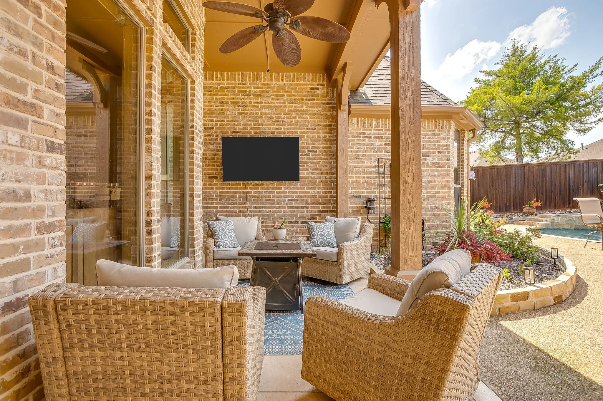 Covered patio featuring a ceiling fan, brick accent wall with mounted display, and a stone-edged planter bed