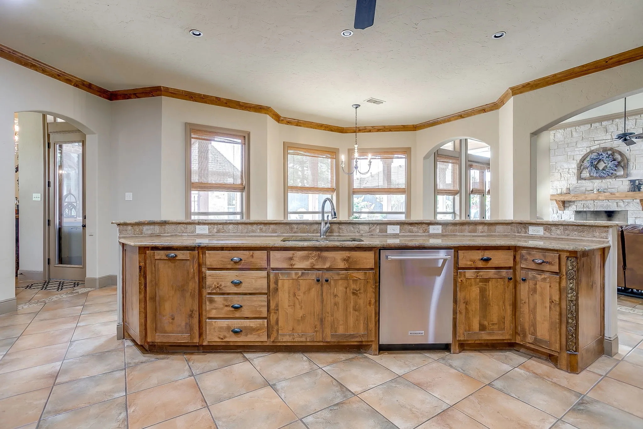 Kitchen island featuring wood cabinetry, stone countertops, an integrated sink, and a stainless steel dishwasher