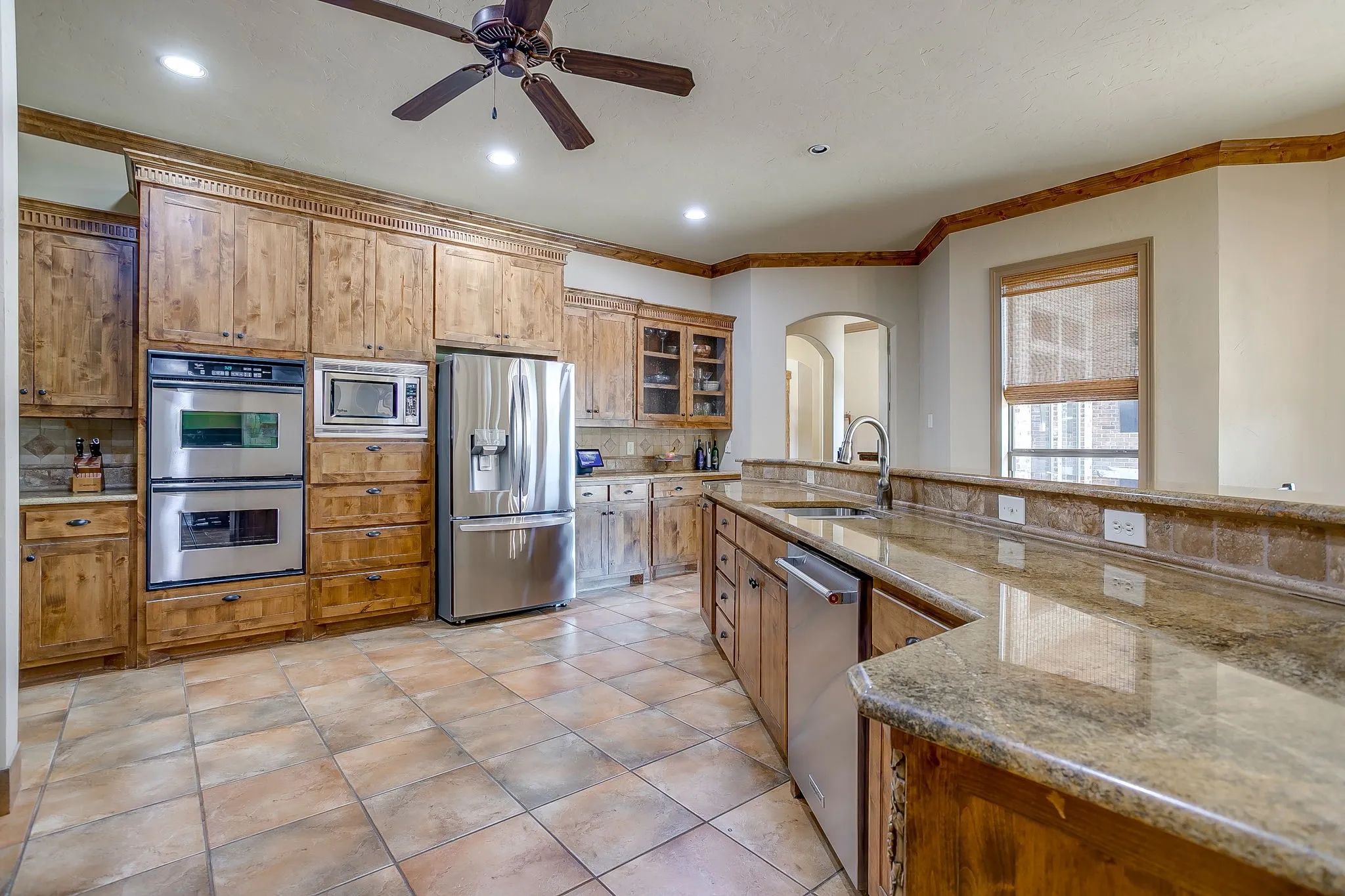 Kitchen featuring extensive wood cabinetry, stainless steel appliances, tile flooring, granite countertops, and a ceiling fan
