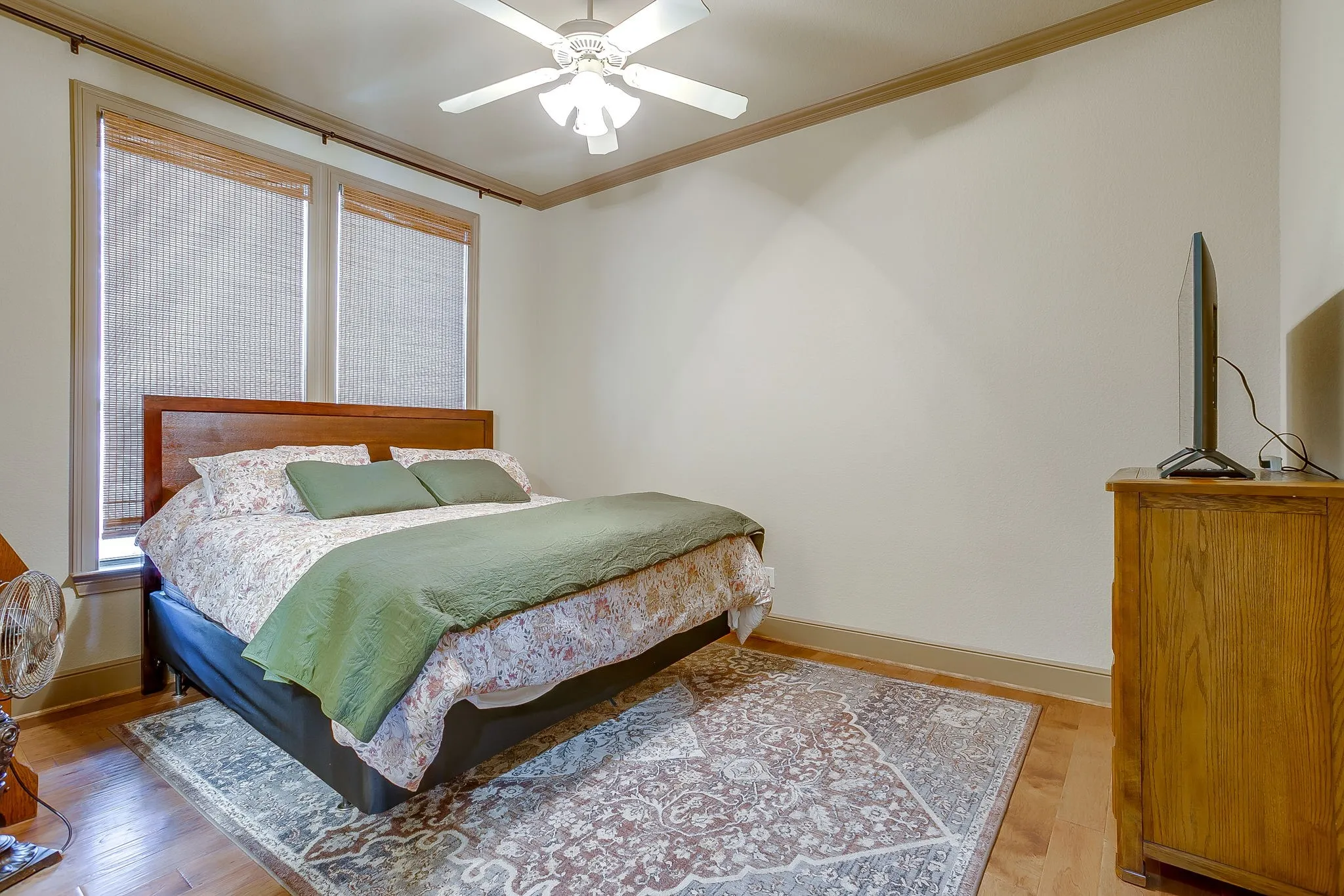 Bedroom #3 featuring wood-finish flooring, two large windows with installed blinds, a ceiling fan with integrated lighting, and crown molding