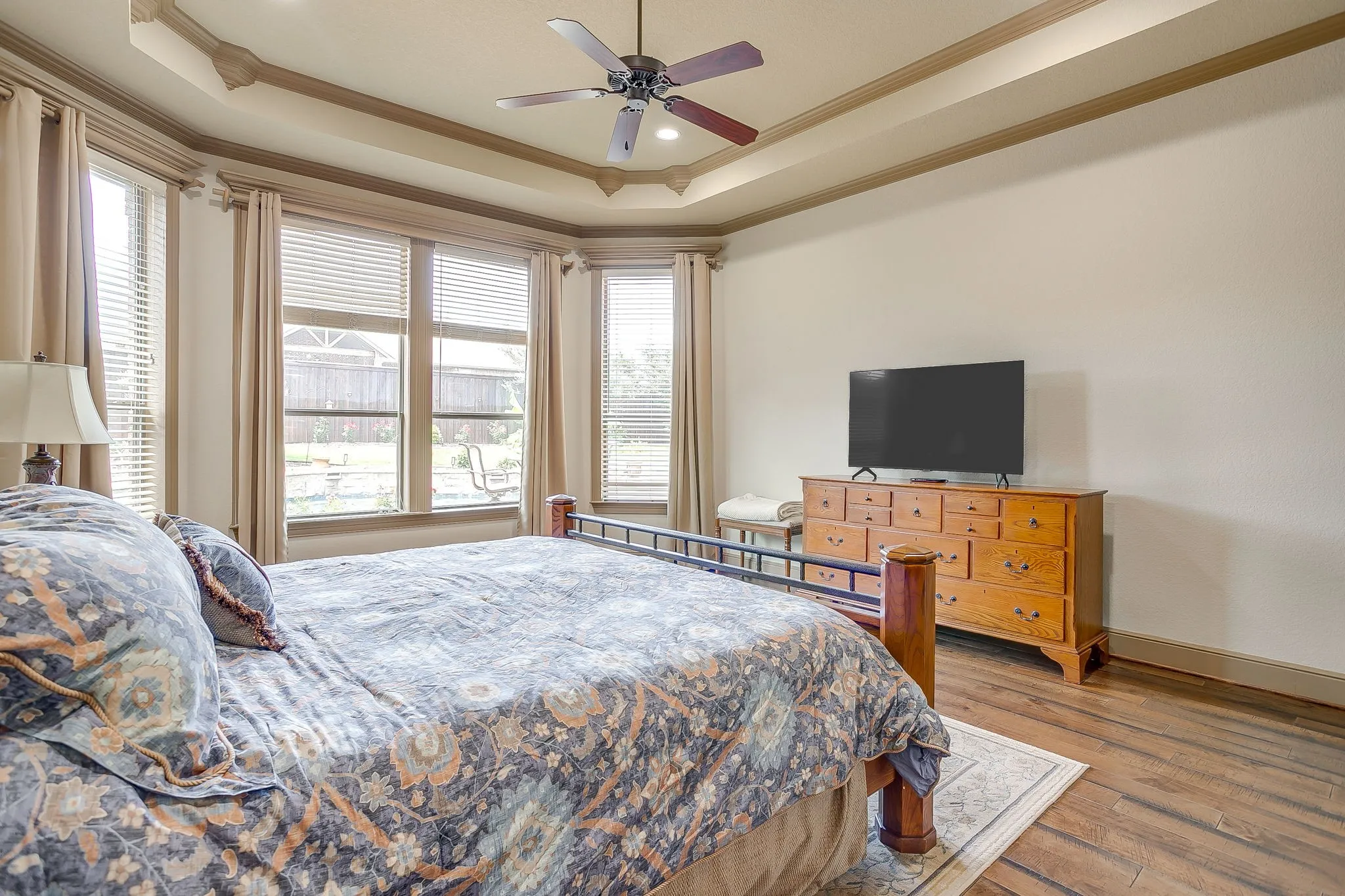 Primary Bedroom featuring wood-finish flooring, a tray ceiling with crown molding, and a ceiling fan