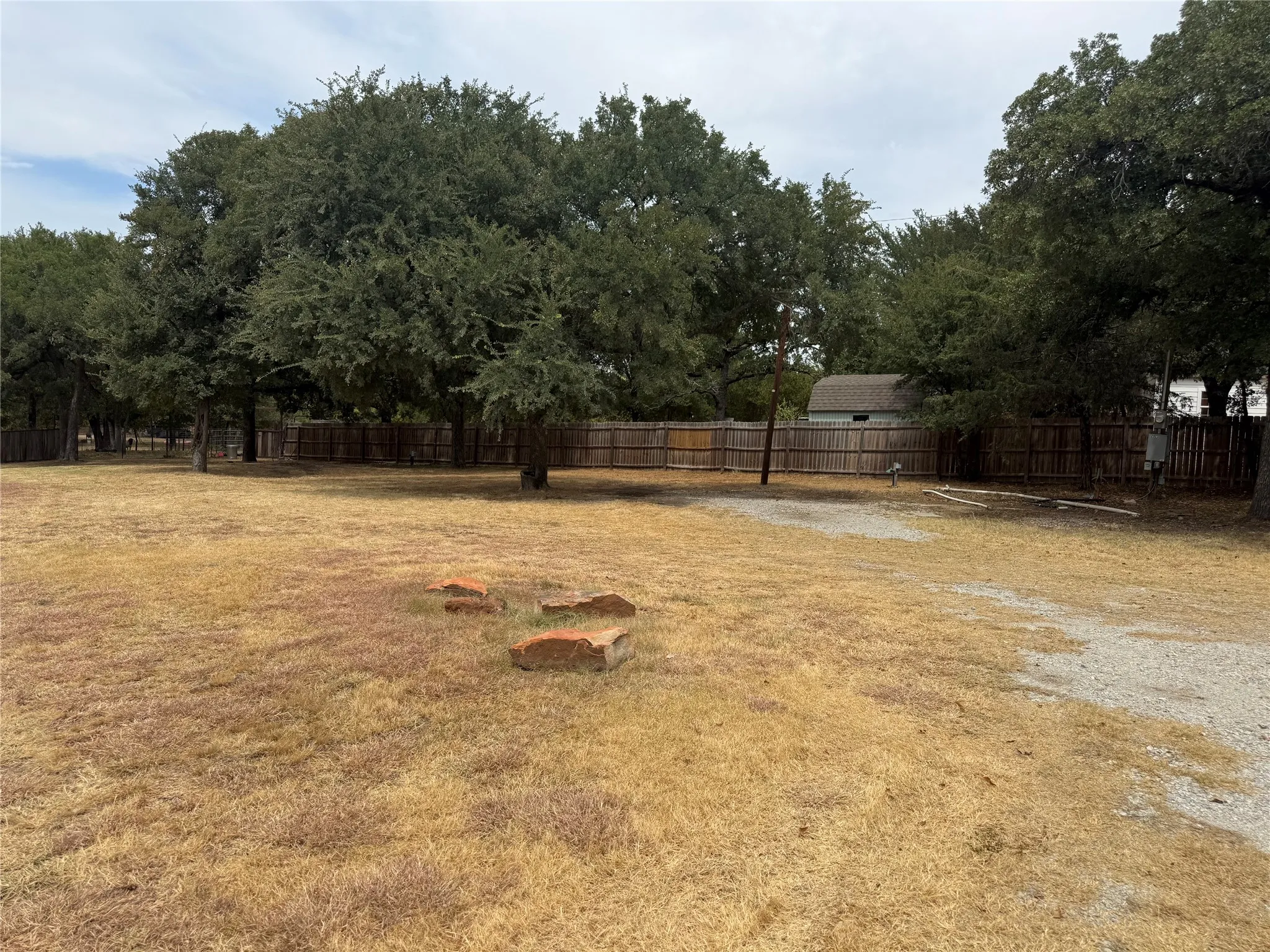 Expansive outdoor area with mature trees, a wood privacy fence, and a gravel surface