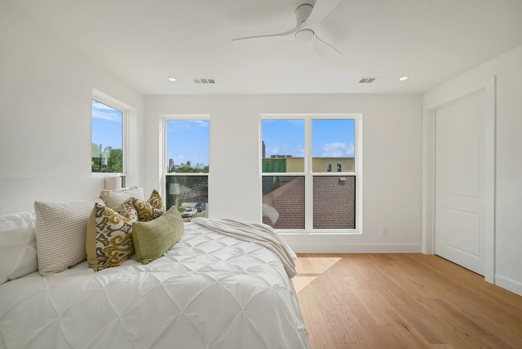 Bright bedroom featuring light wood-finish flooring and multiple windows