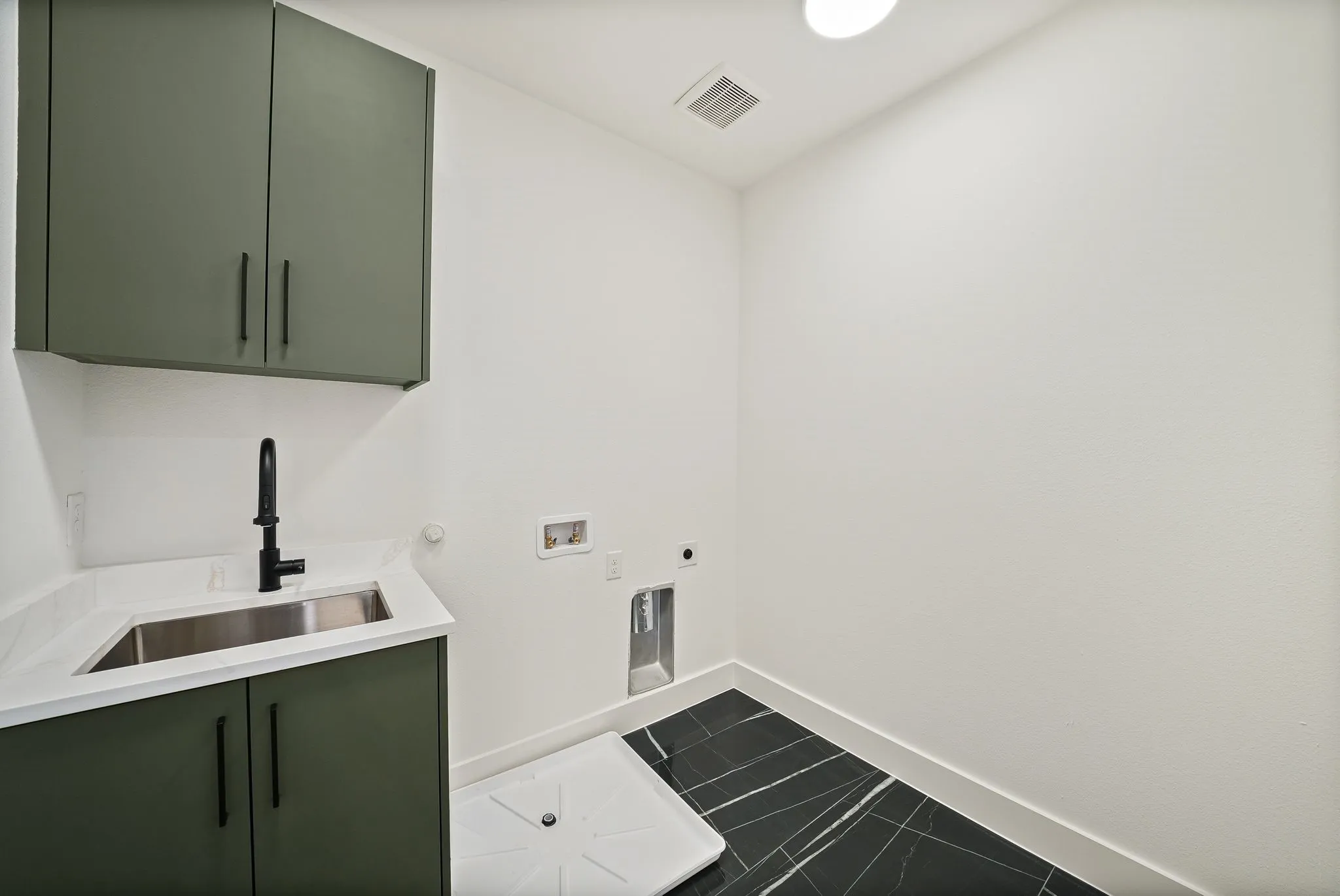 Dedicated laundry area featuring a utility sink, white countertop, and dark green cabinetry