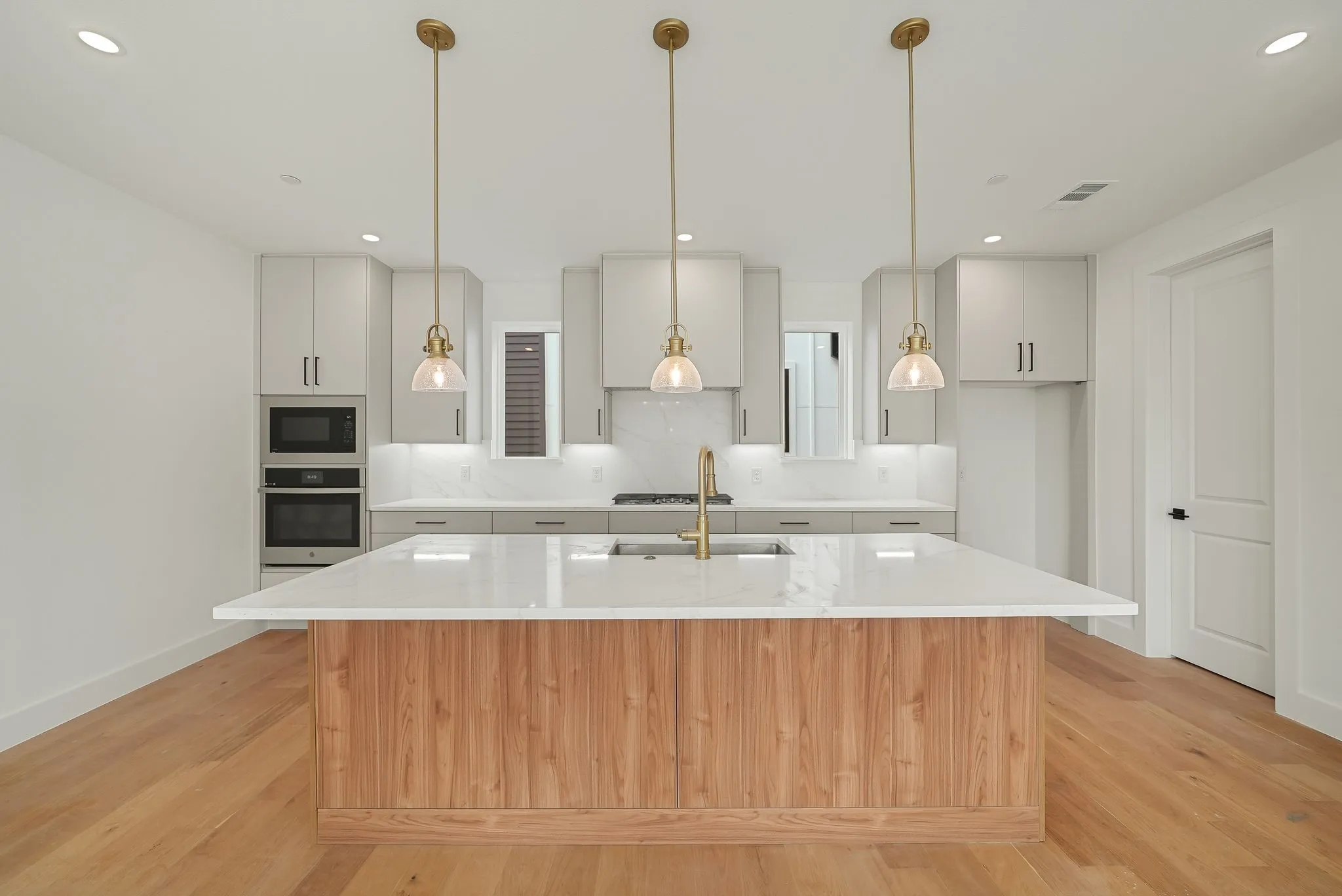 Kitchen featuring a wood-finish island with a white countertop, light gray cabinetry, built-in stainless steel appliances, and wood-finish flooring