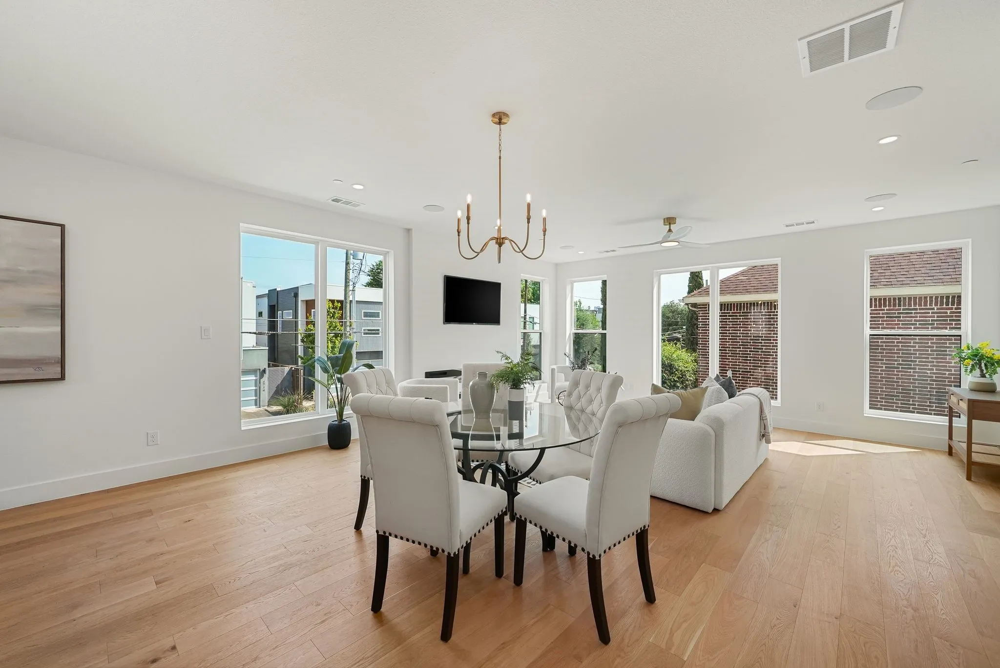 Open-concept living space with light wood-finish flooring, numerous windows, and a modern chandelier